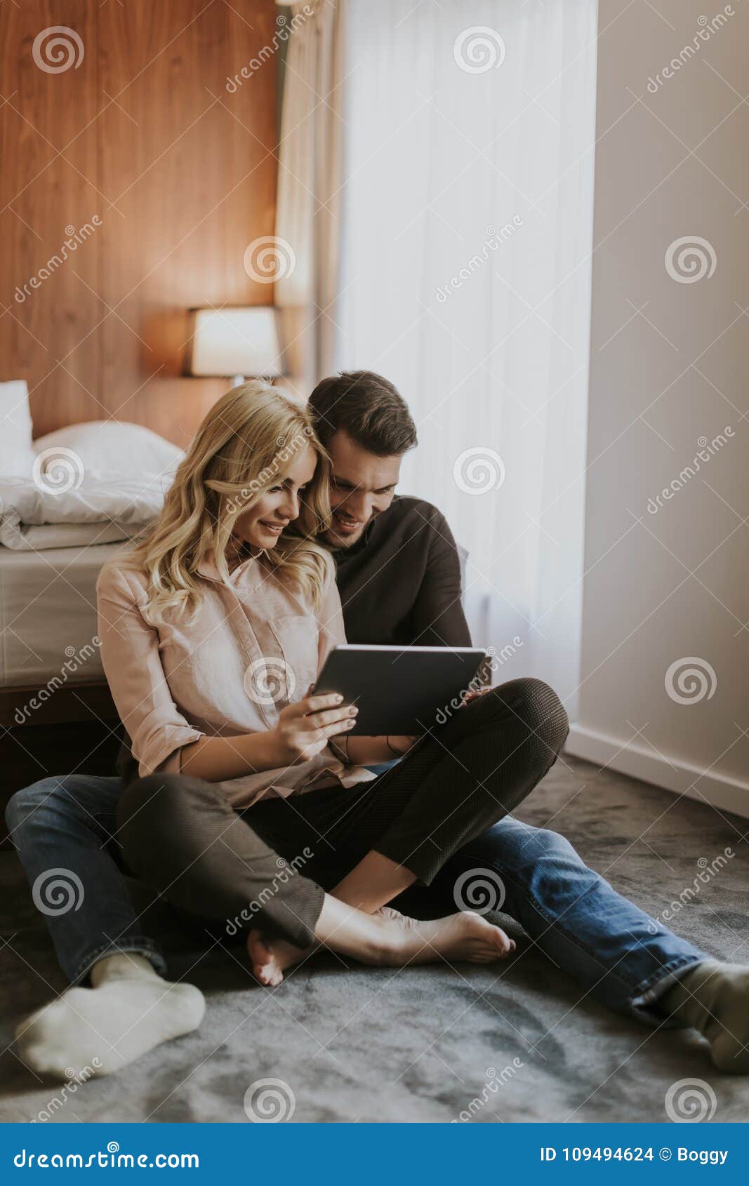Loving Couple Sitting On The Floor In Bedroom And Usin