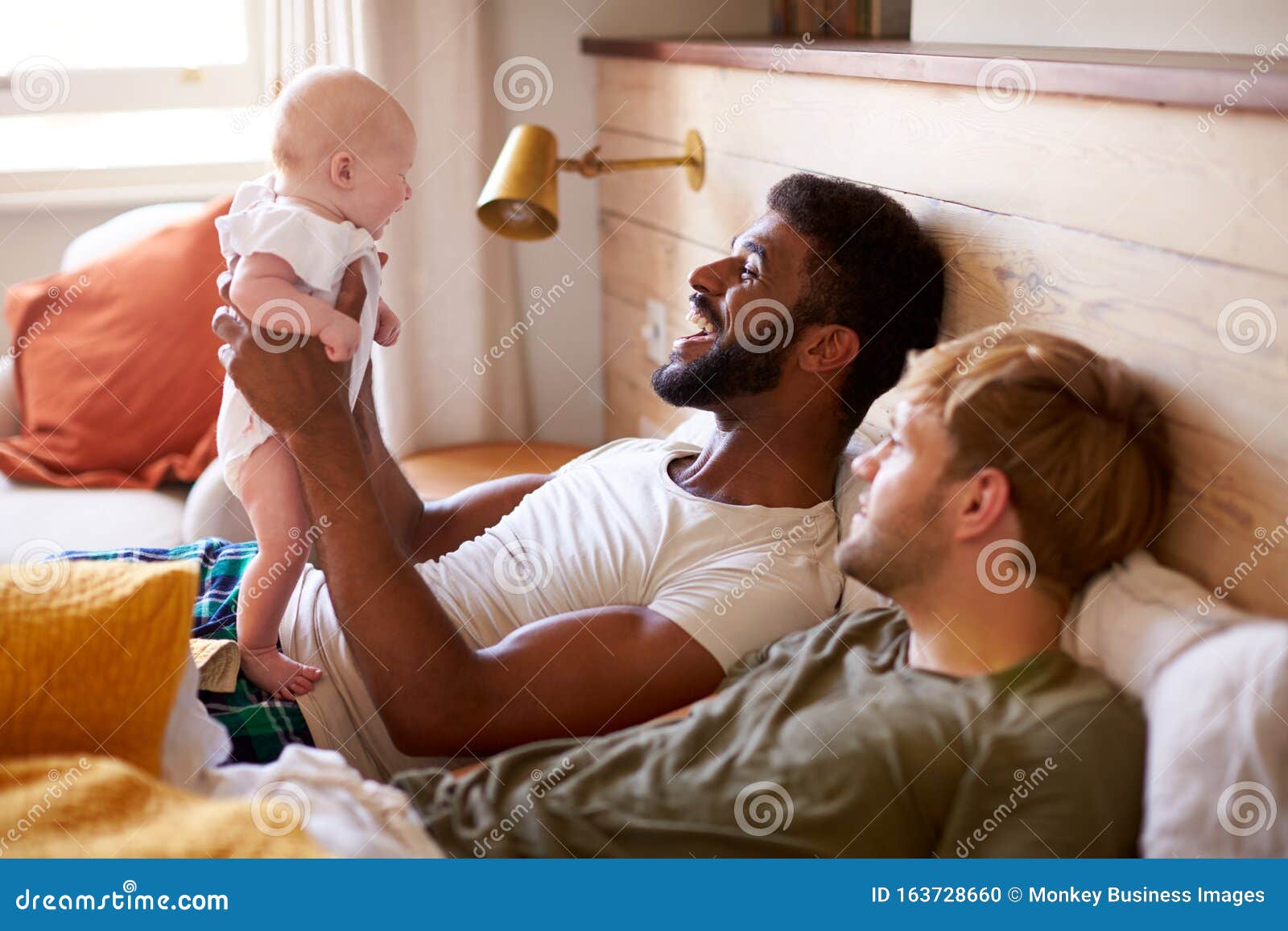 Loving Male Same Sex Couple Cuddling Baby Daughter in Bedroom at Home Together Stock Photo pic