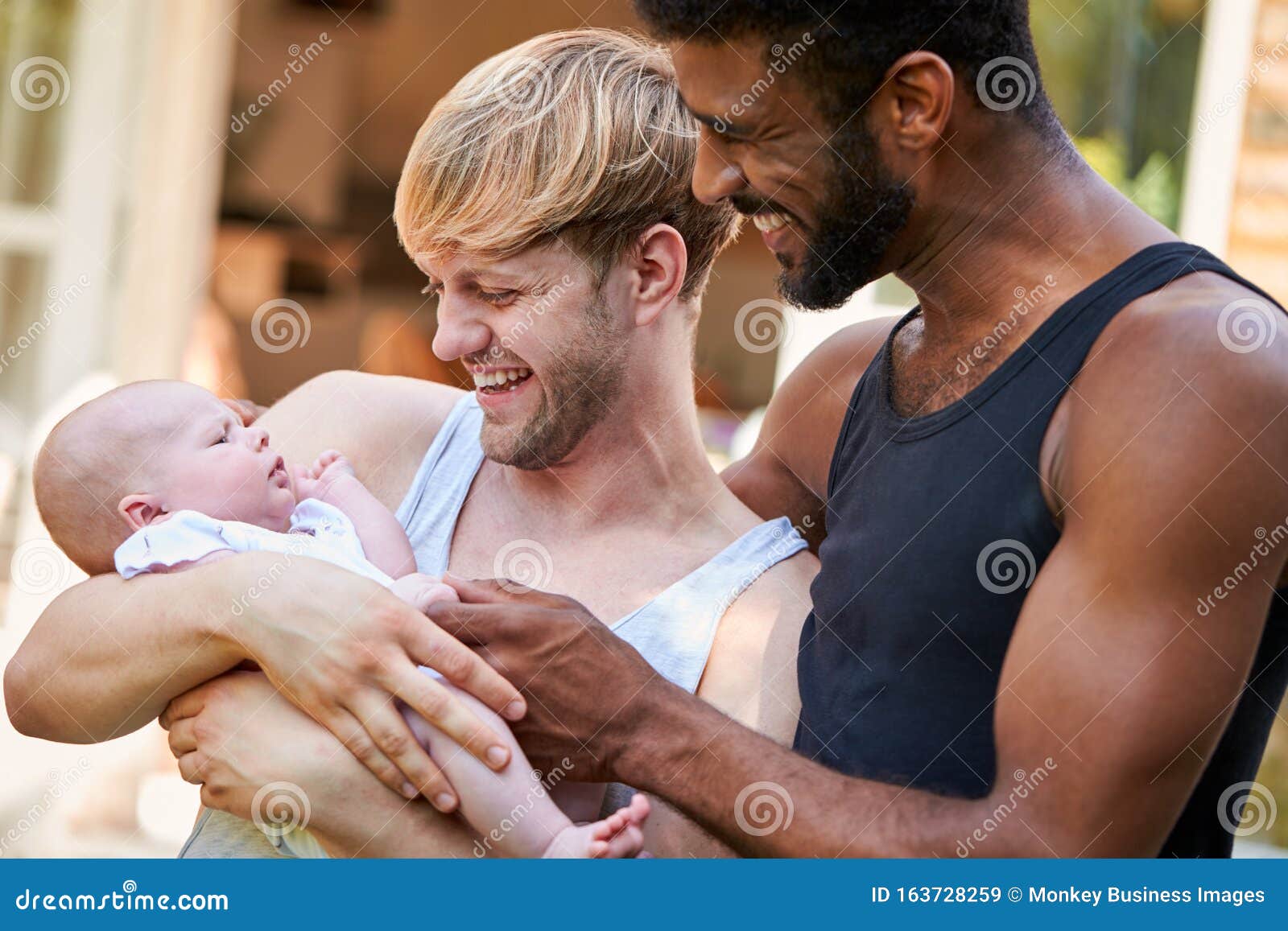 Loving Male Same Sex Couple Cuddling Baby Daughter at Home in Garden Together Stock Image