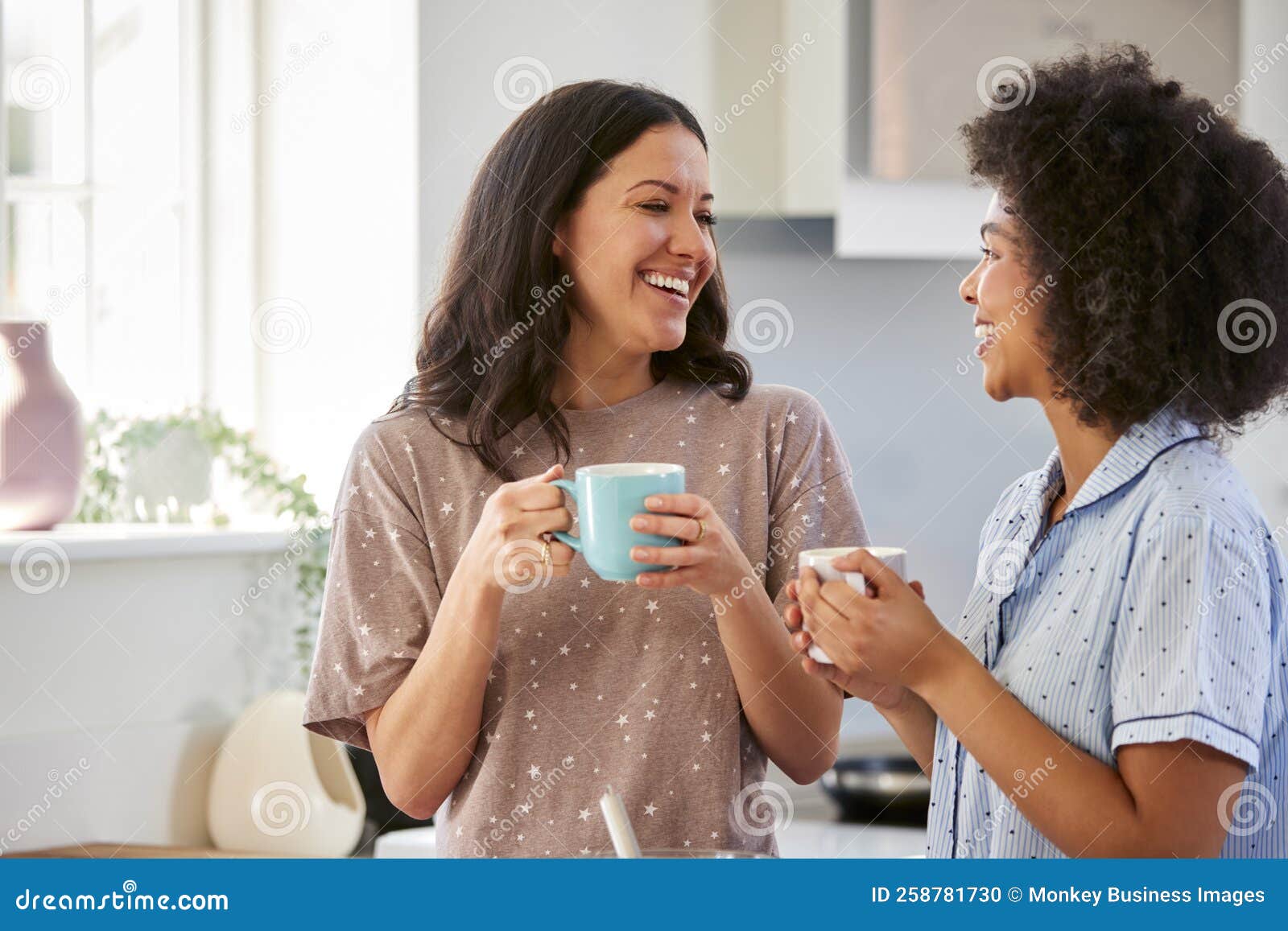 Loving Same Sex Female Couple Wearing Pyjamas Making Morning Pancakes in Kitchen at Home Stock Photo