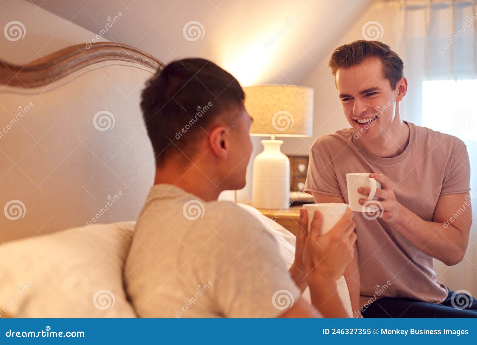 Loving Same Sex Male Couple in Bed at Home Drinking Hot Drink Together Stock Image