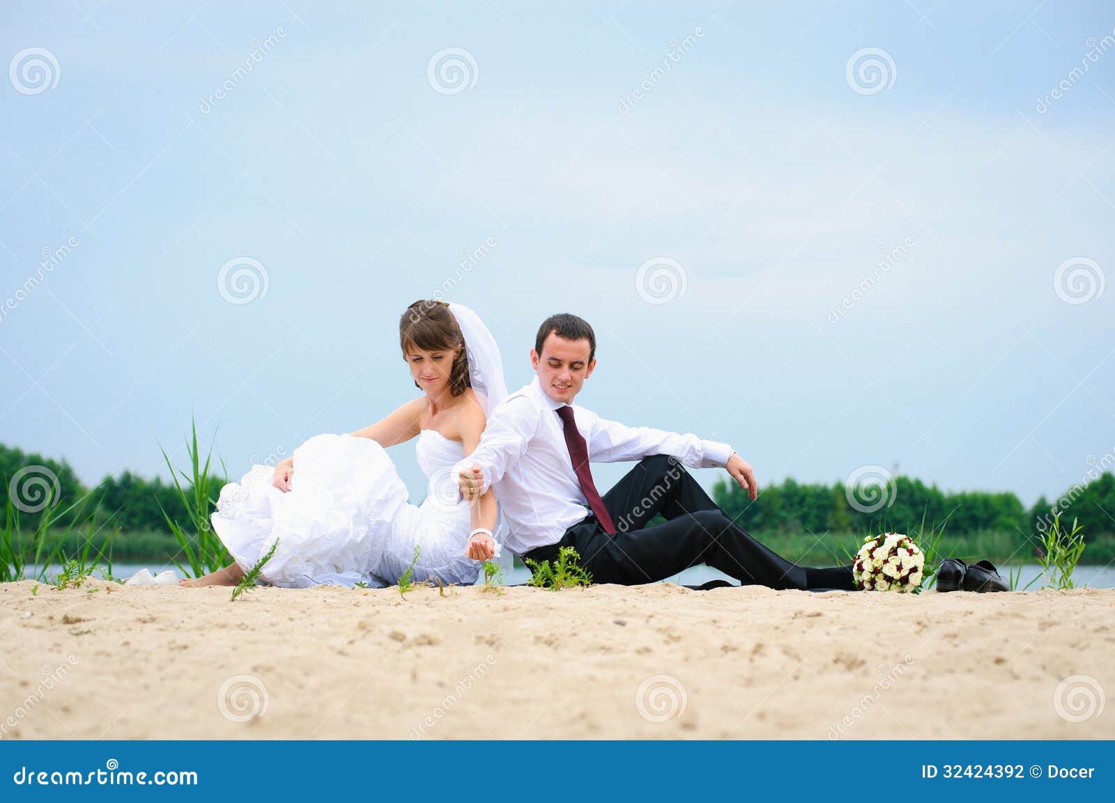 loving wedding couple sitting near water and strew sands