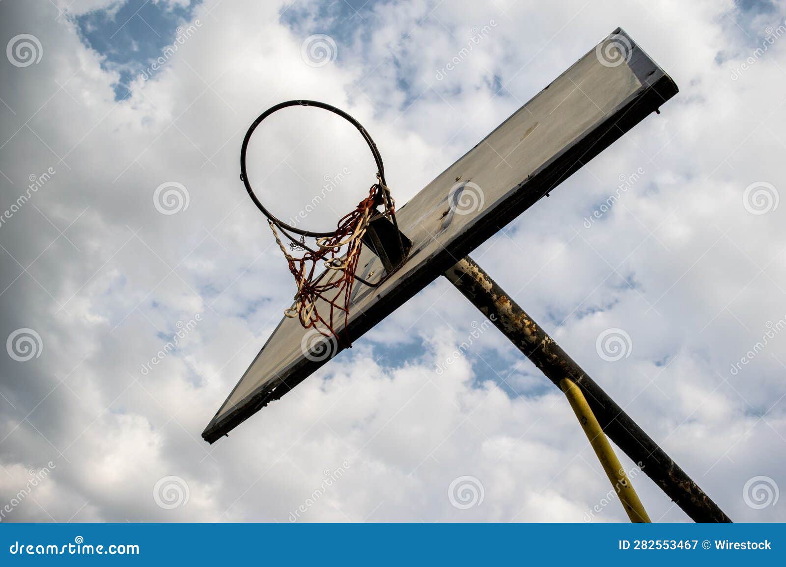 Low Angle Shot of a Rusty Old Basketball Hoop Under a Cloudy Blue Sky