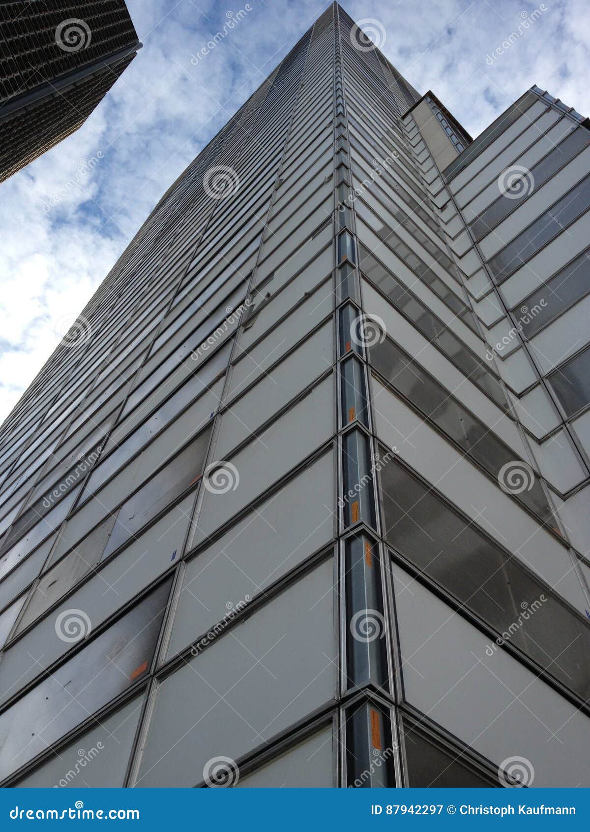 Low angle view of a modern business building with grey facade made of glass against cloudy sky