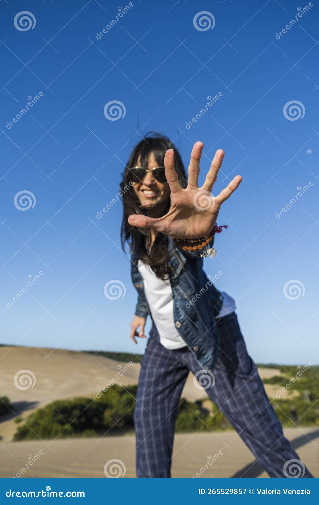 low angle view of a similing woman showing the palm of her hand in a dune. stop gesture