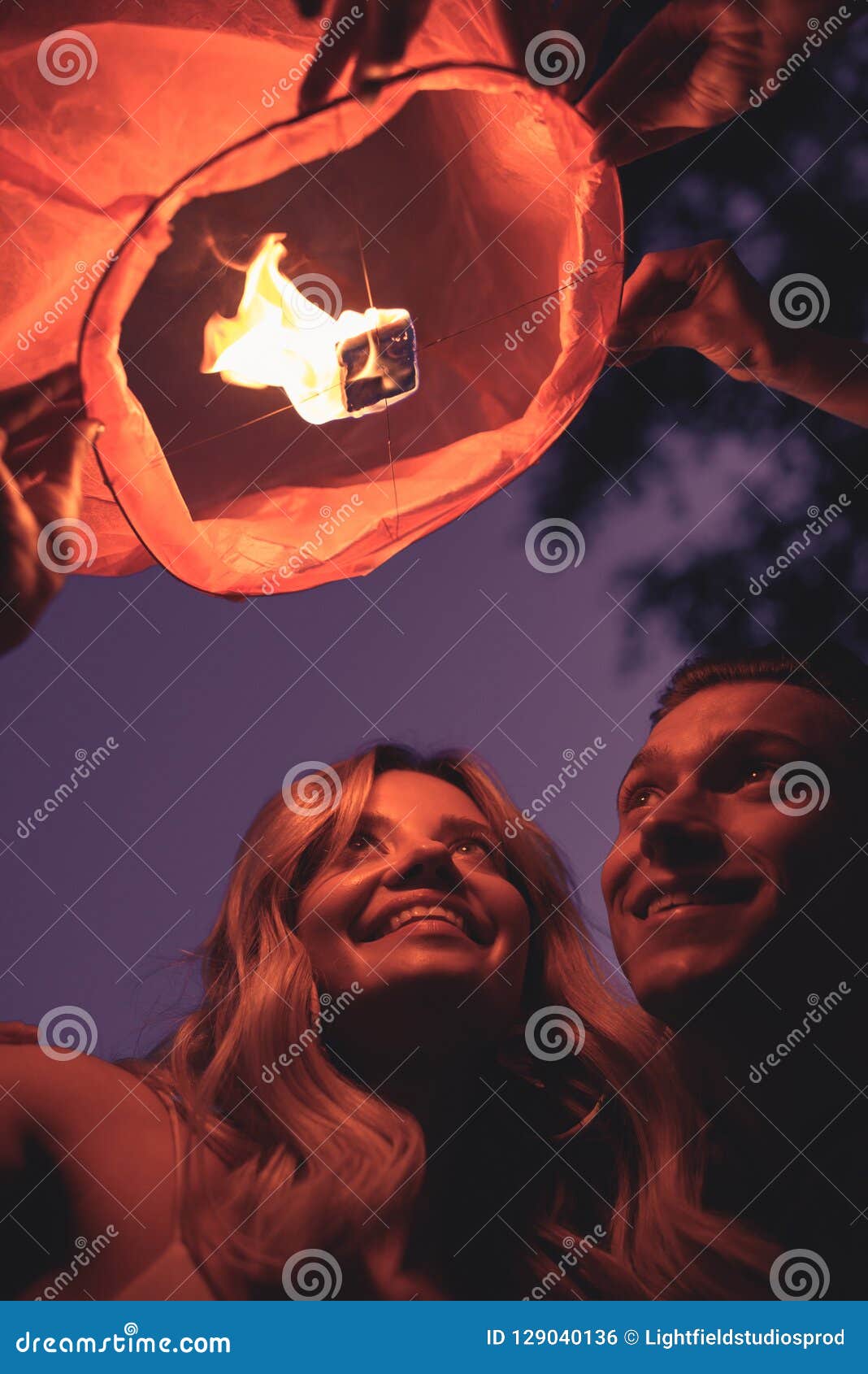 low angle view of smiling young couple launching sky lantern on river beach