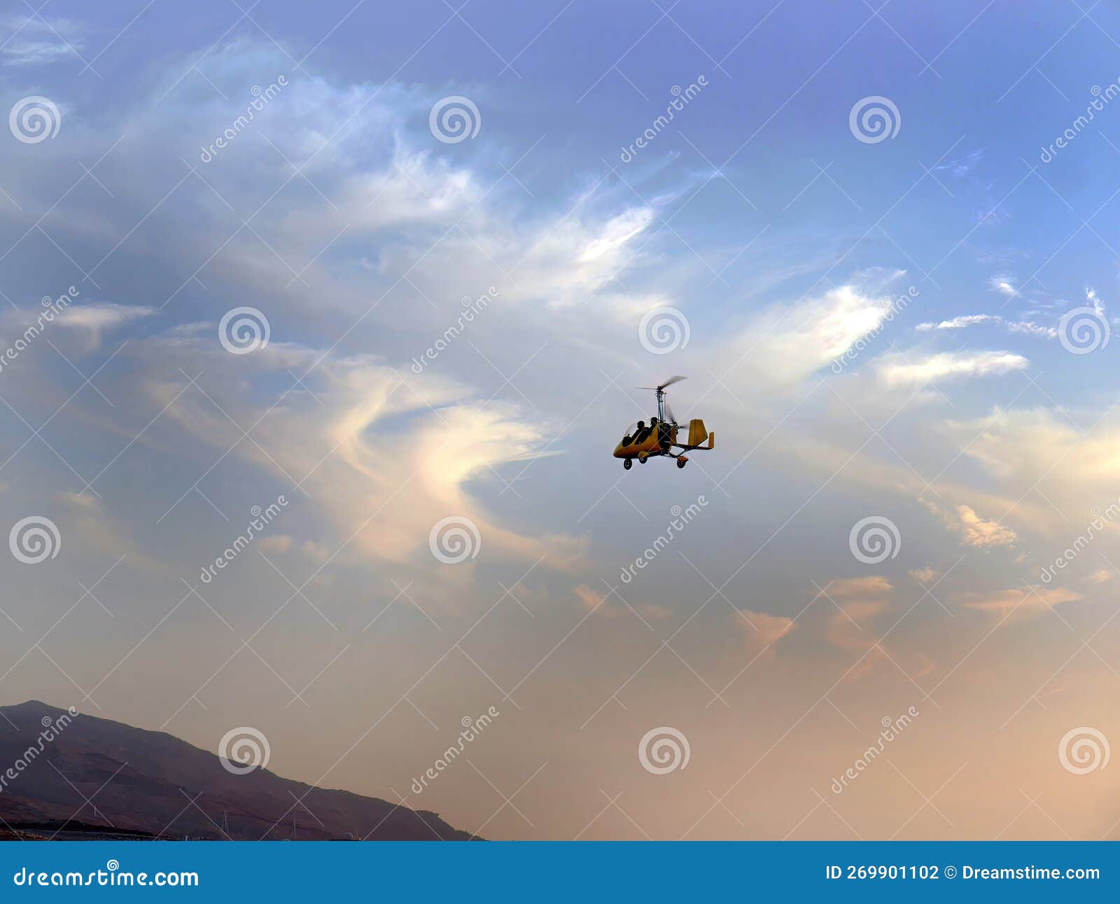 low angle view of yellow color gyrocopter flying in the blue sky and dramatic clouds, fun fly, aero sports, skydive, roto craft,