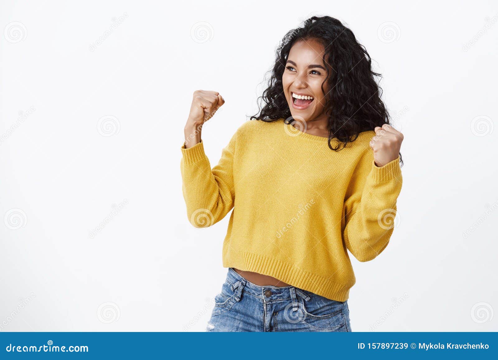 lucky venturous young african-american girl fan in yellow sweater, making fist pump gesture as smiling and looking left