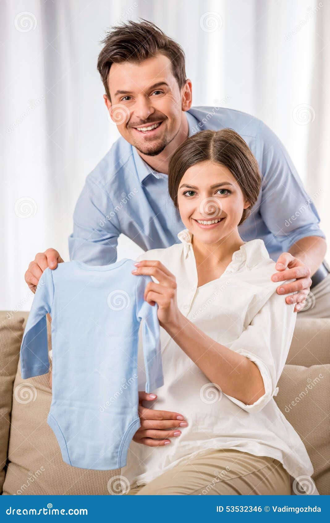 Lycklig familj. Lyckliga unga föräldrar rymmer deras framtida babys kläder