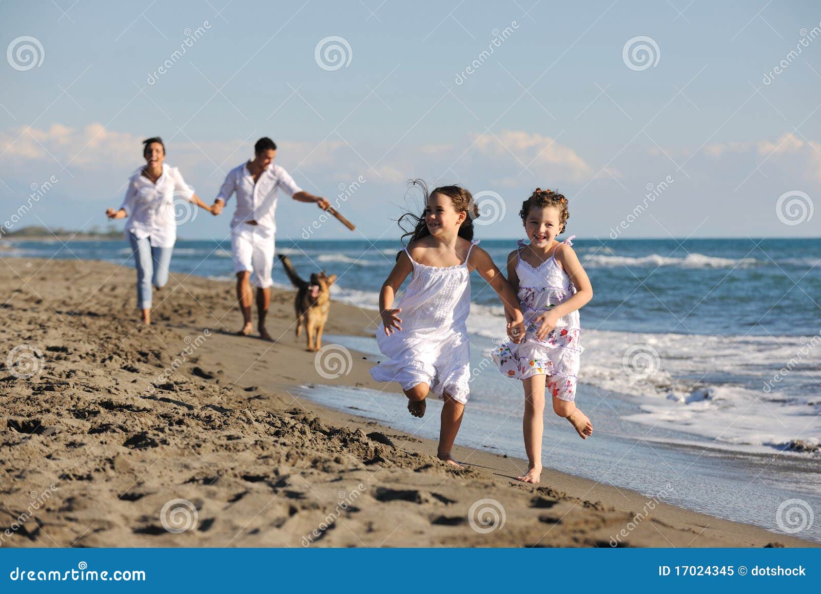 Lycklig familj som leker med hunden på strand. Den lyckliga unga familjen i vita kläder har gyckel och spelrum med den härliga hunden på semestrar på härlig strand