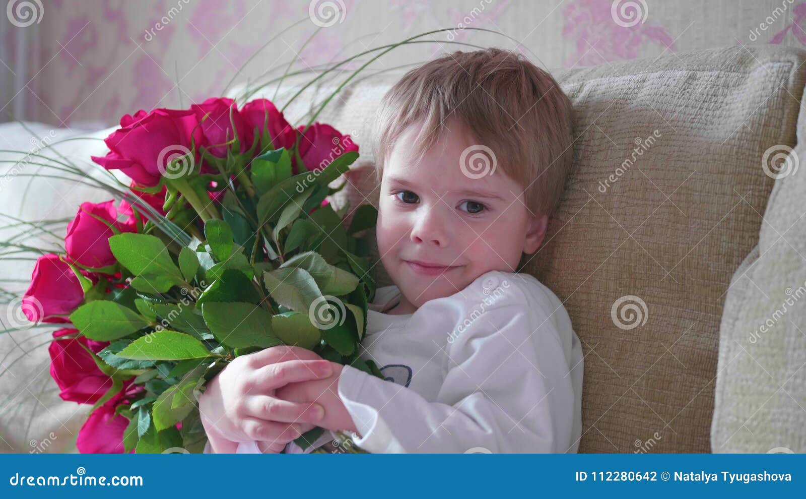 Lyckligt behandla som ett barn rymma en stor bukett av scharlakansröda rosor En gåva för födelsedag för moder` s. Barnet rymmer en stor bukett av scharlakansröda rosor