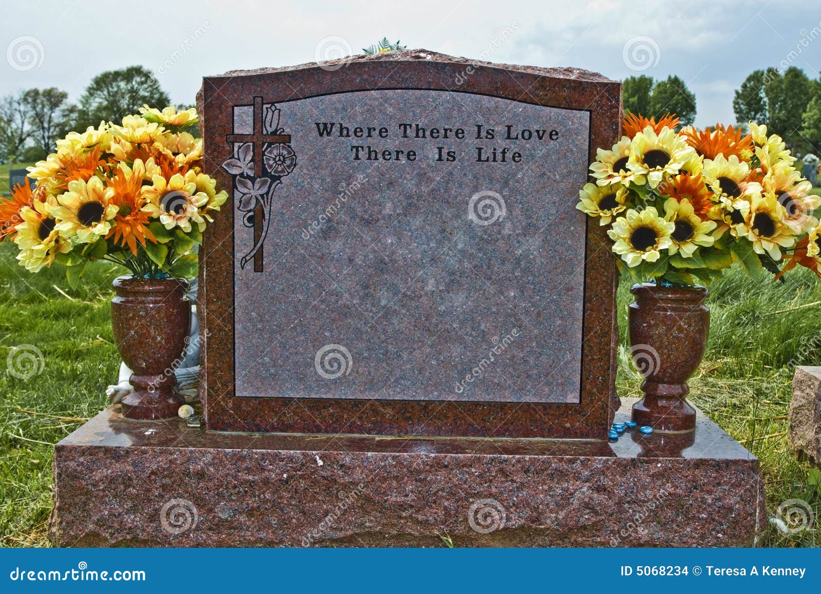 Pierre commémorative faite de granit rouge. L'inscription s'affiche : Là où il y a amour il y a durée. Fleurs de source/été dans les vases. L'ornement dans le coin gauche supérieur est une croix avec des fleurs.