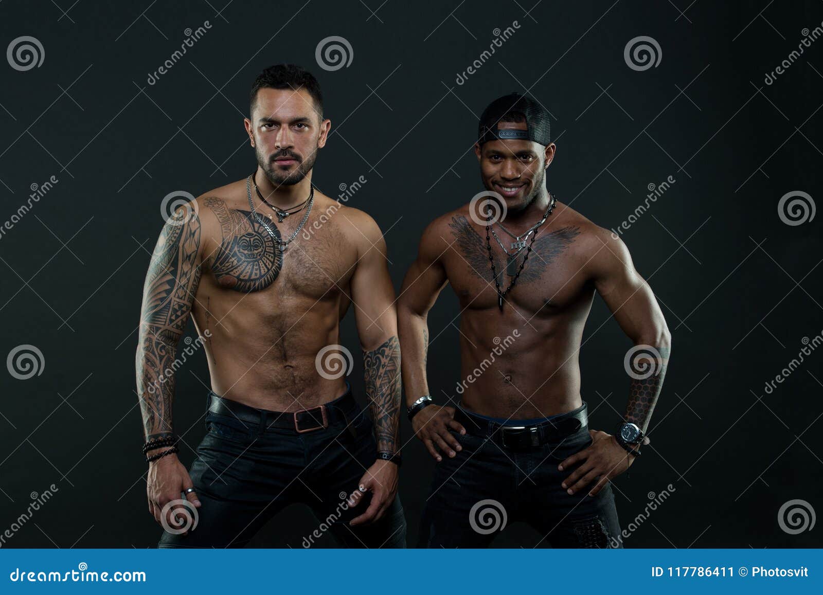 machos with muscular tattooed torsos look attractive, dark background. athletes on confident faces with nude muscular