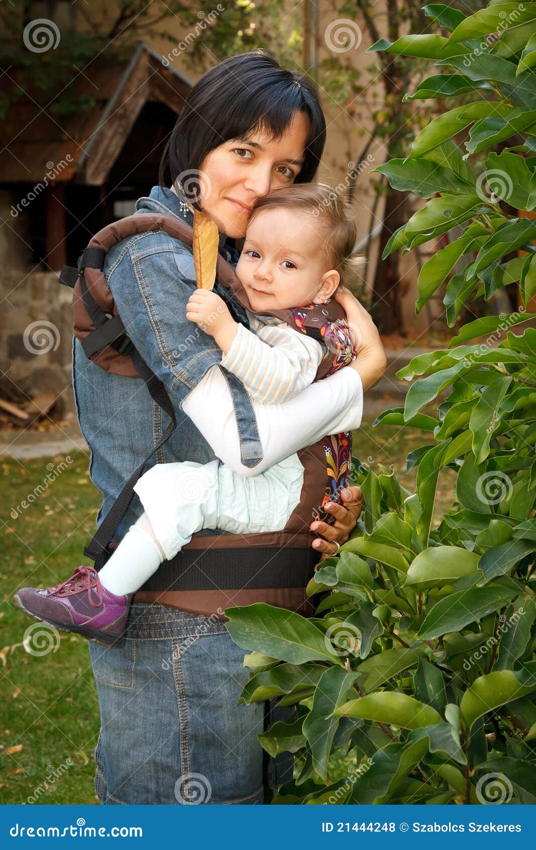 Madre con il bambino in imbracatura. Generi il trasporto del suo bambino bello in imbracatura, all'esterno