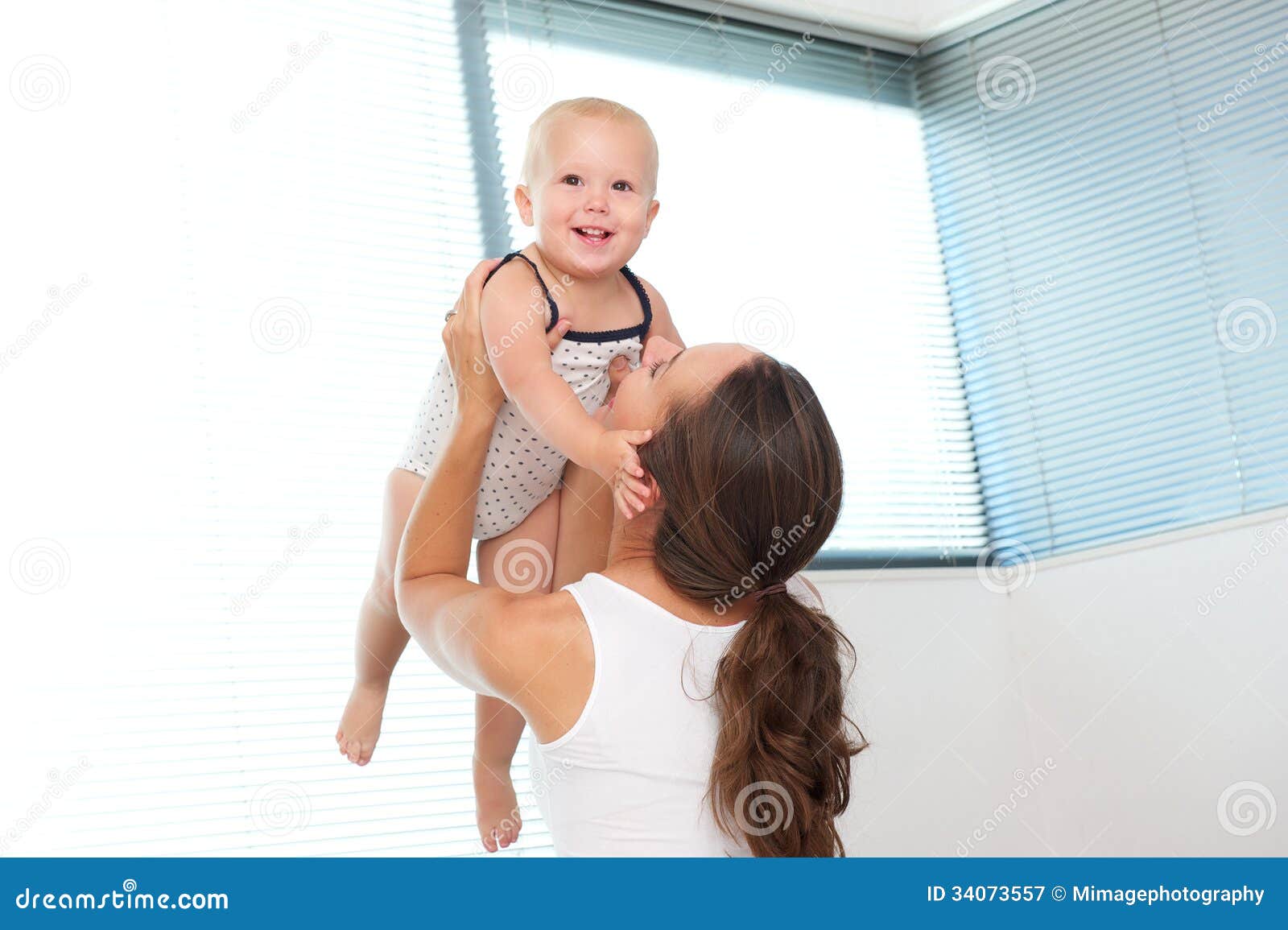 Retrato de una madre feliz que levanta encima de bebé lindo en casa