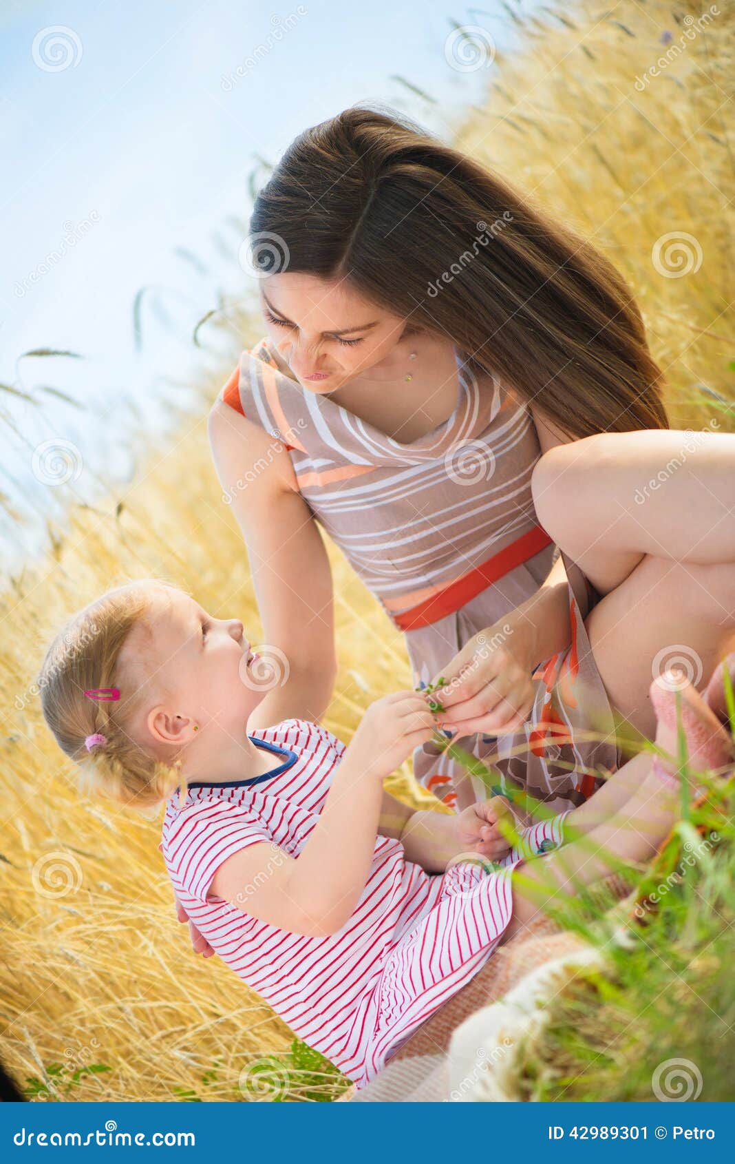 Madre joven con la pequeña hija en el campo de trigo. Madre bastante joven con la pequeña hija linda en el campo de trigo