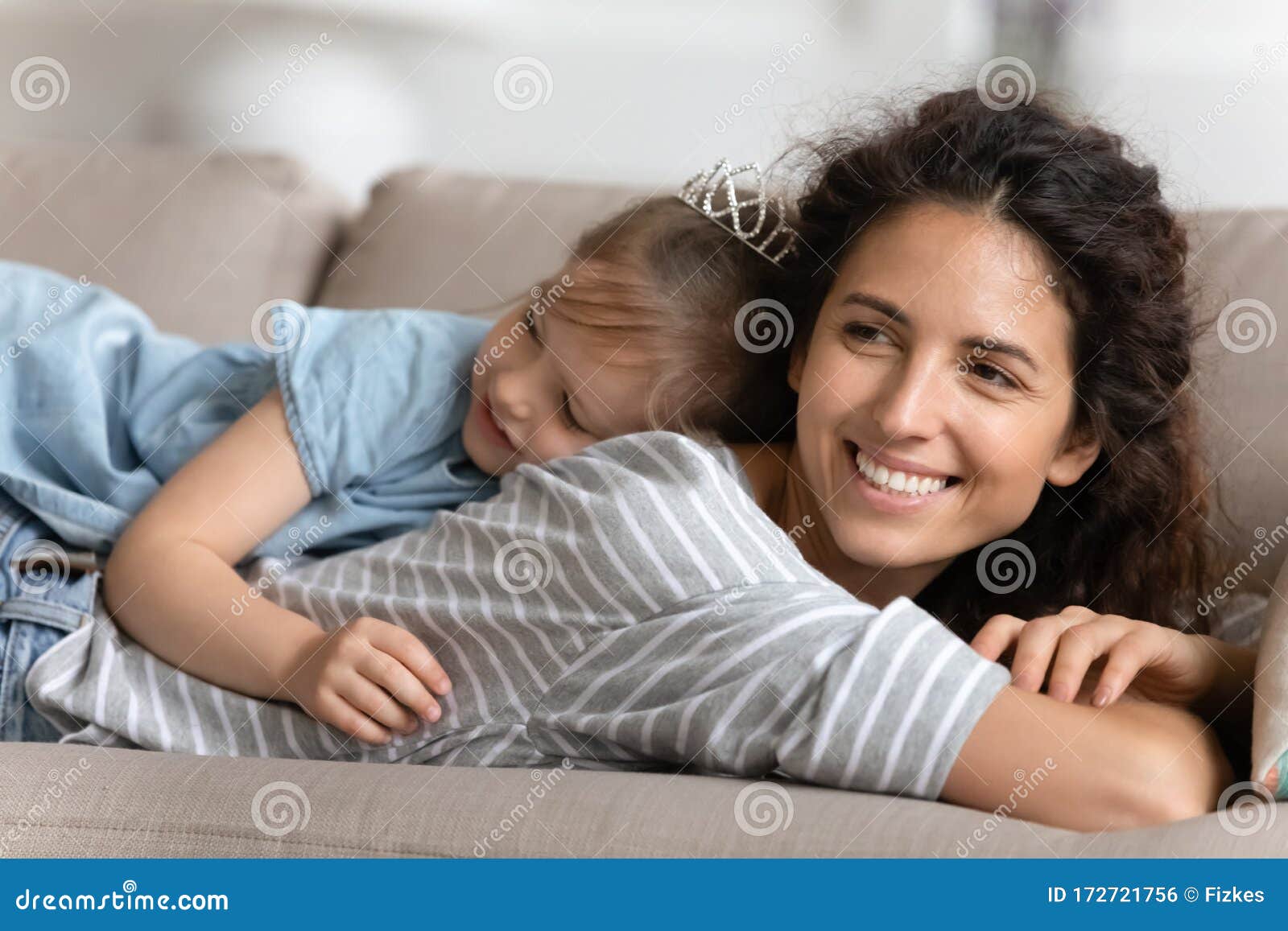 Madre Joven Sonriente Descansando En El Sofá Con Su Hija En La Espalda Foto De Archivo Imagen