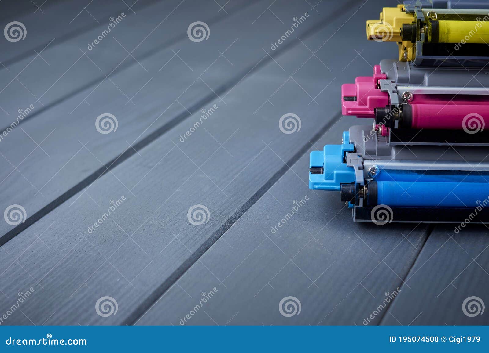 magenta, cyan and yellow toner cartridges for color laser printers stacked on gray wooden background