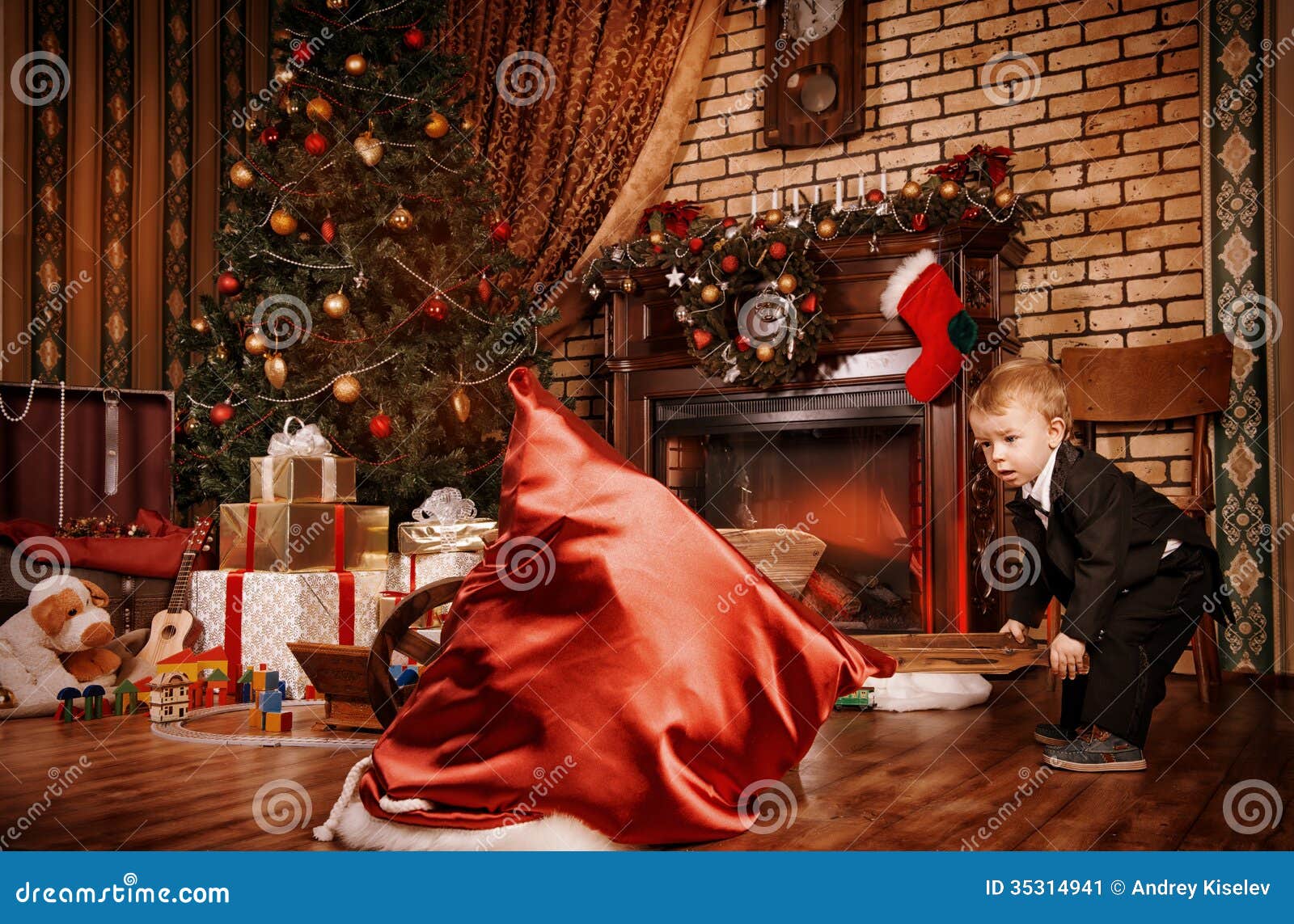 Magische Zeit. Kleiner Junge, der zu Hause mit Spielwaren nahe dem Kamin und dem Weihnachtsbaum spielt.