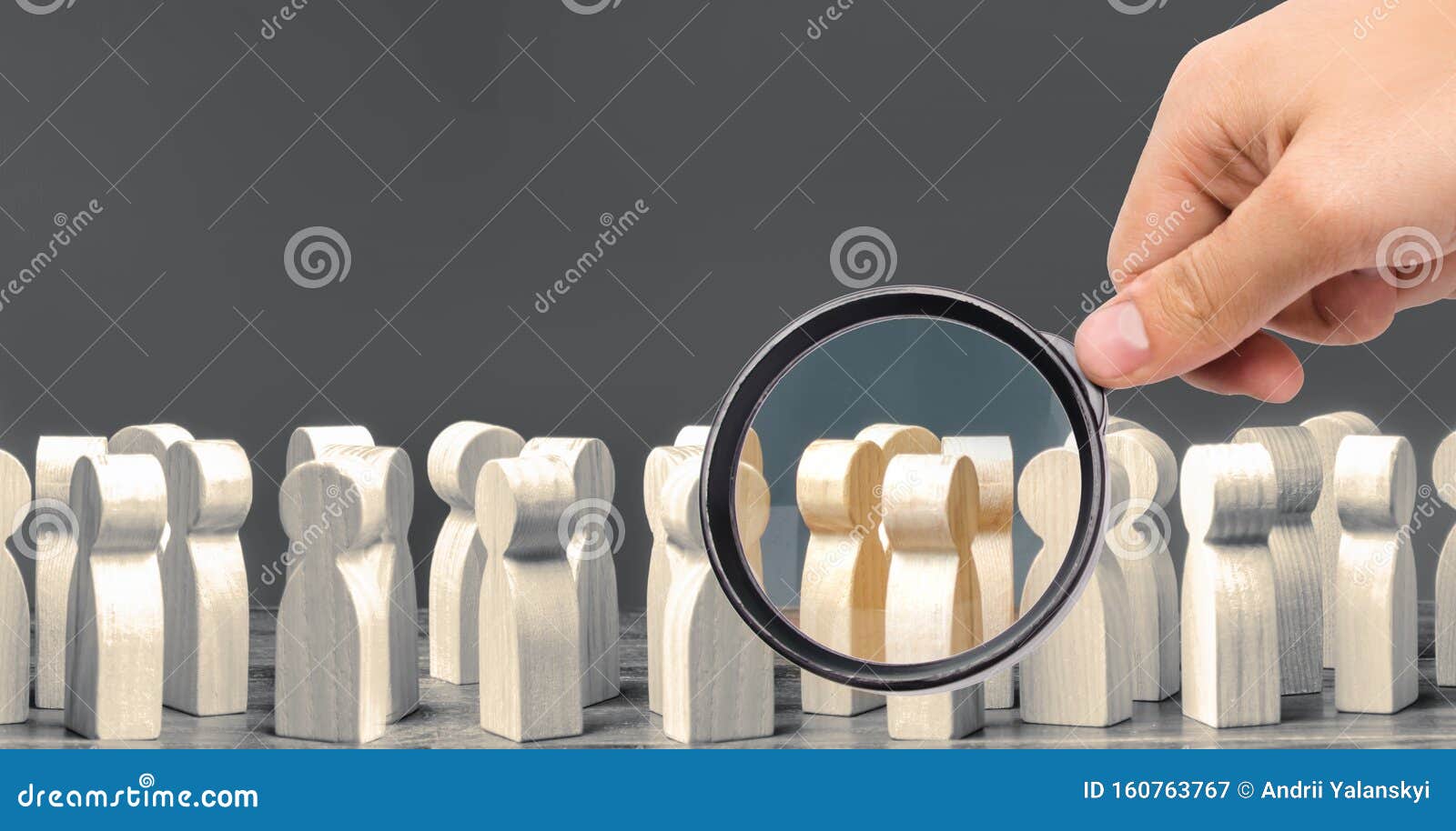 a magnifying glass looks at a crowd of wooden figures of people. society, demographic. group of citizens, rally, political