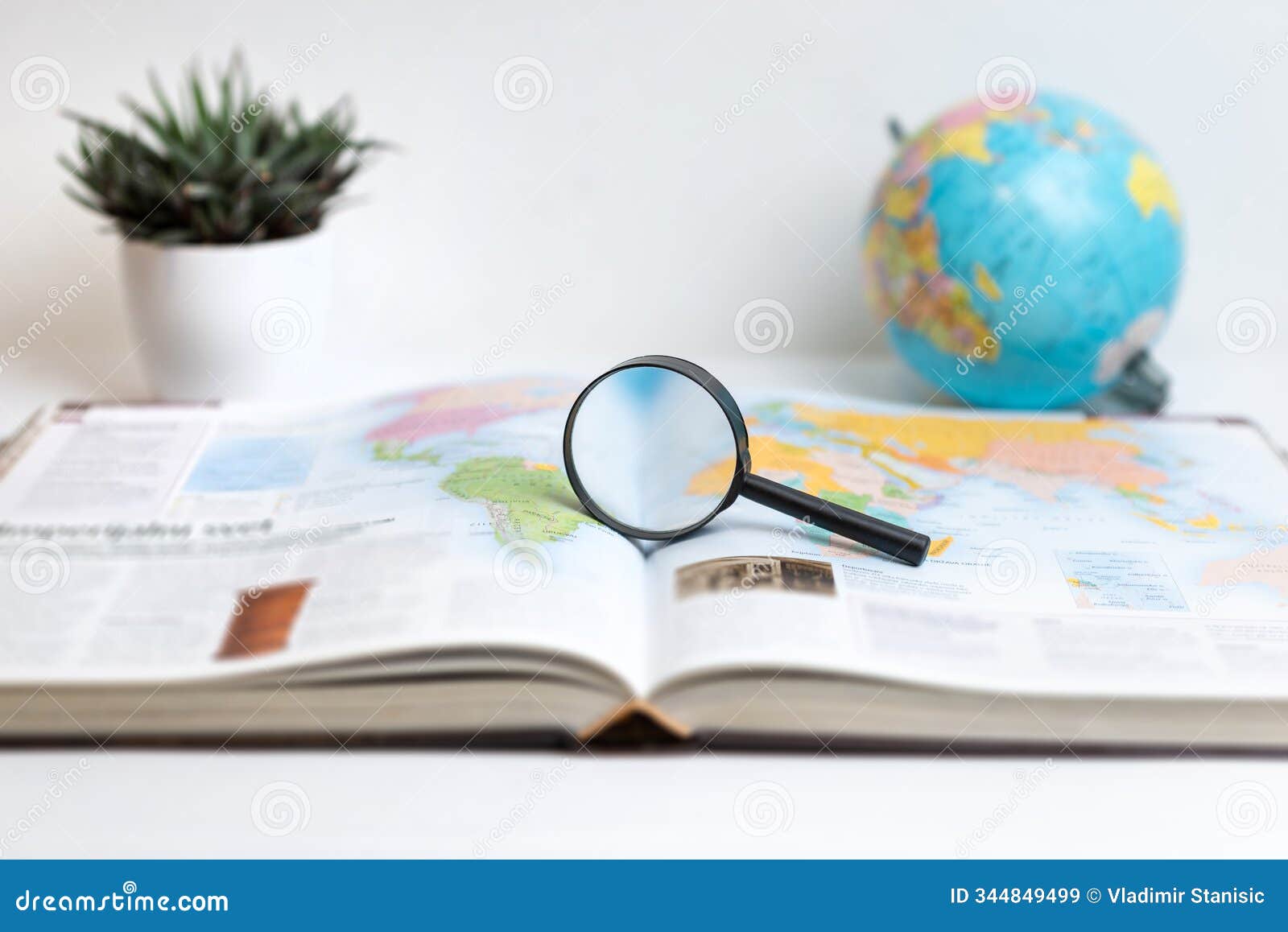 magnifying glass on open book displaying world map with globe in background