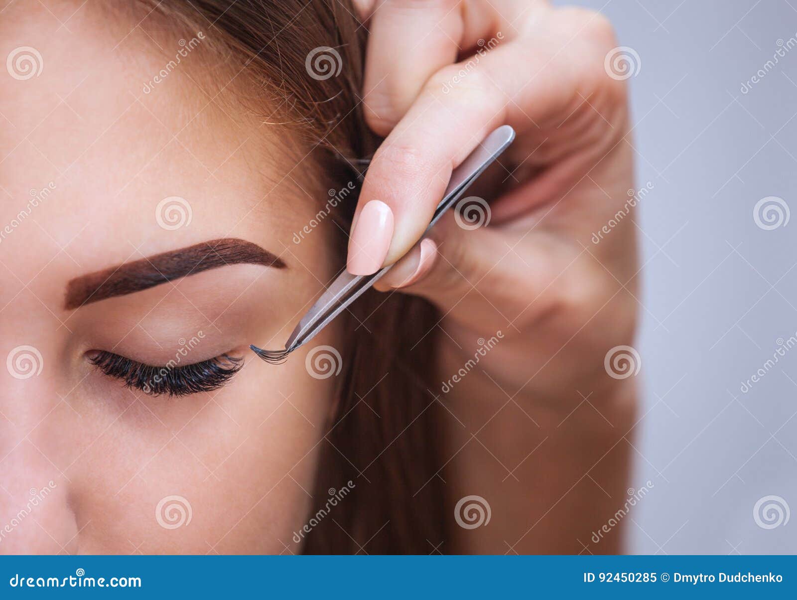 makeup master corrects, and strengthens eyelashes beams, holding out a pair of tweezers in a beauty salon