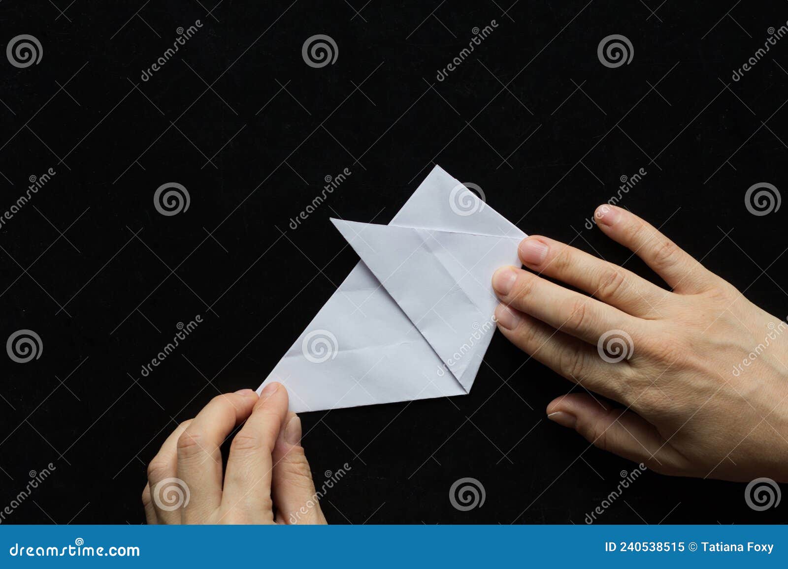 making snowflake. step 6. woman hands folding one third of triangle sheet of paper over on the black background