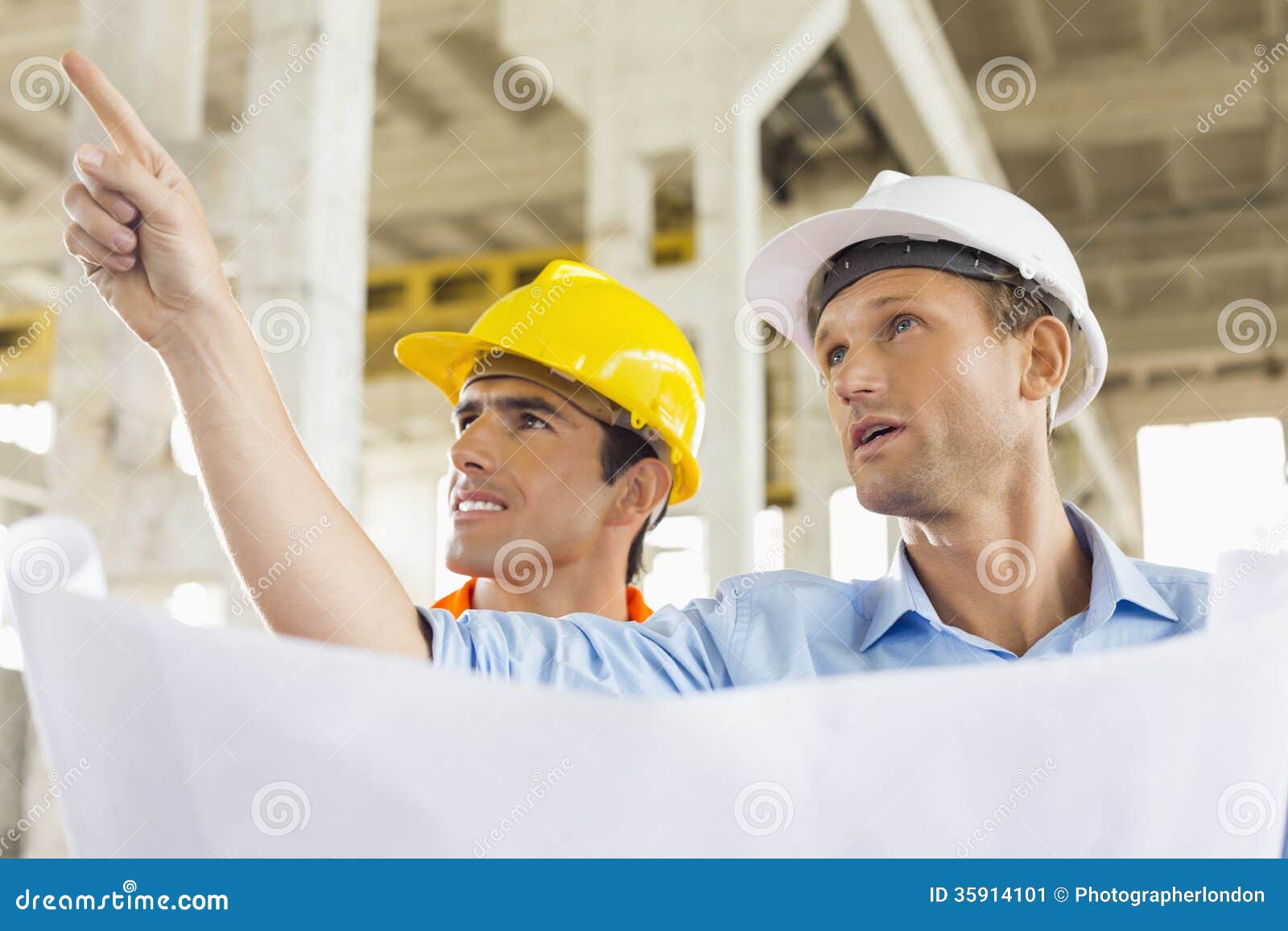 male architect explaining building plan to colleague at construction site