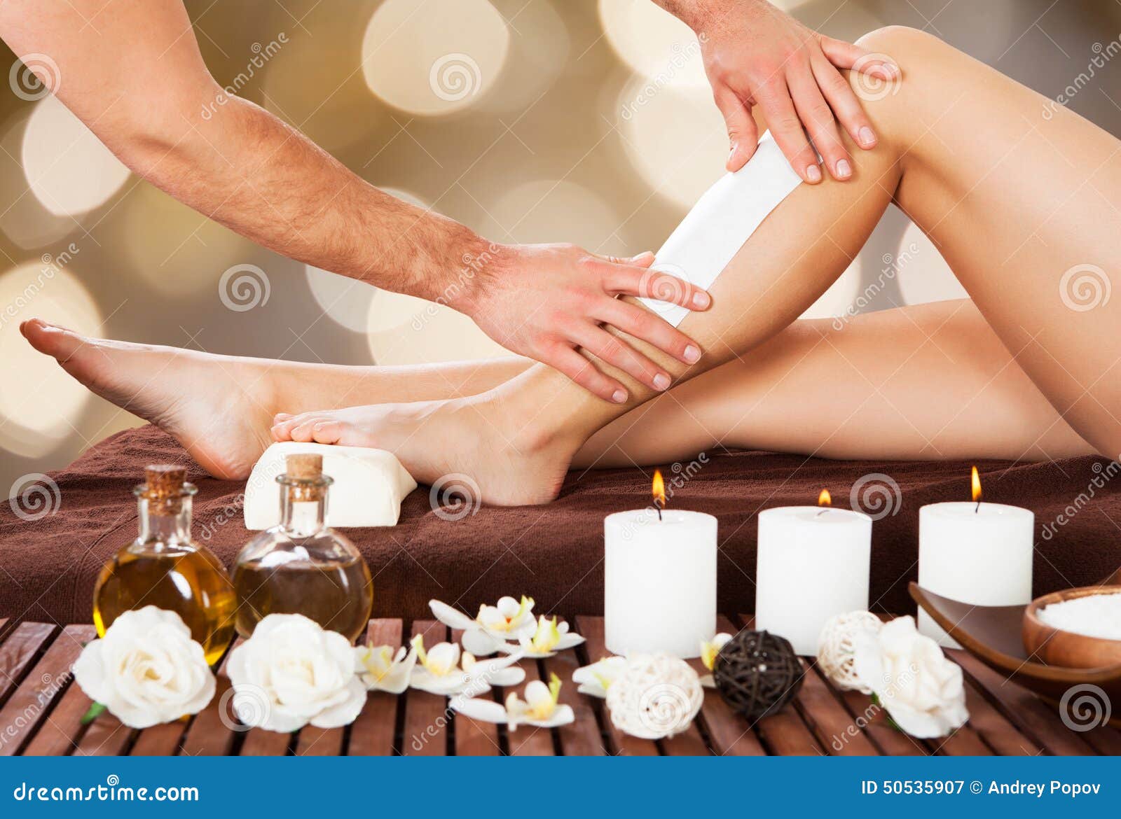 male beautician waxing woman's leg in spa