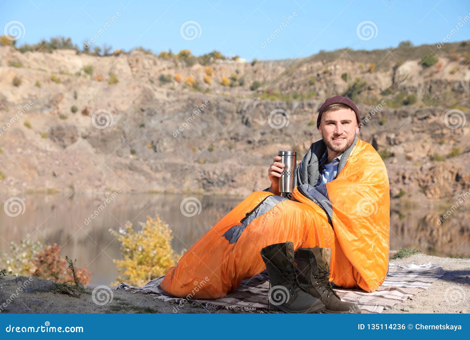 Male Camper with Thermos in Sleeping Bag Outdoors. Stock Photo Image