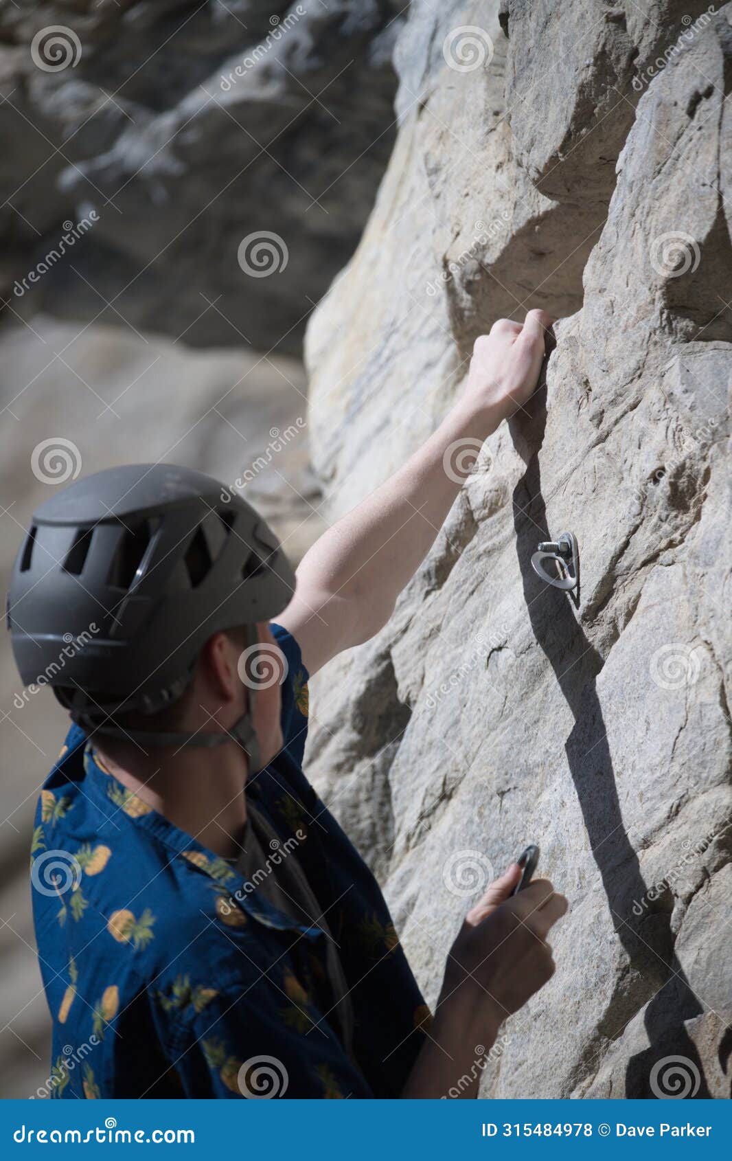 male climber about to hook quick draw to pin on rock face