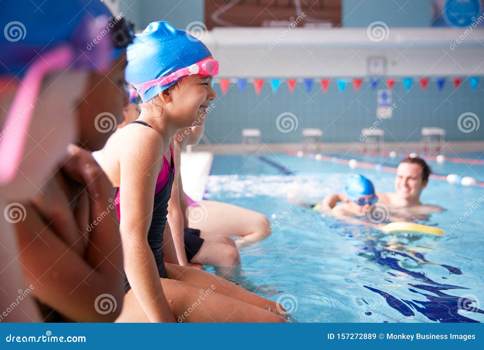male coach in water giving group of children swimming lesson in indoor pool