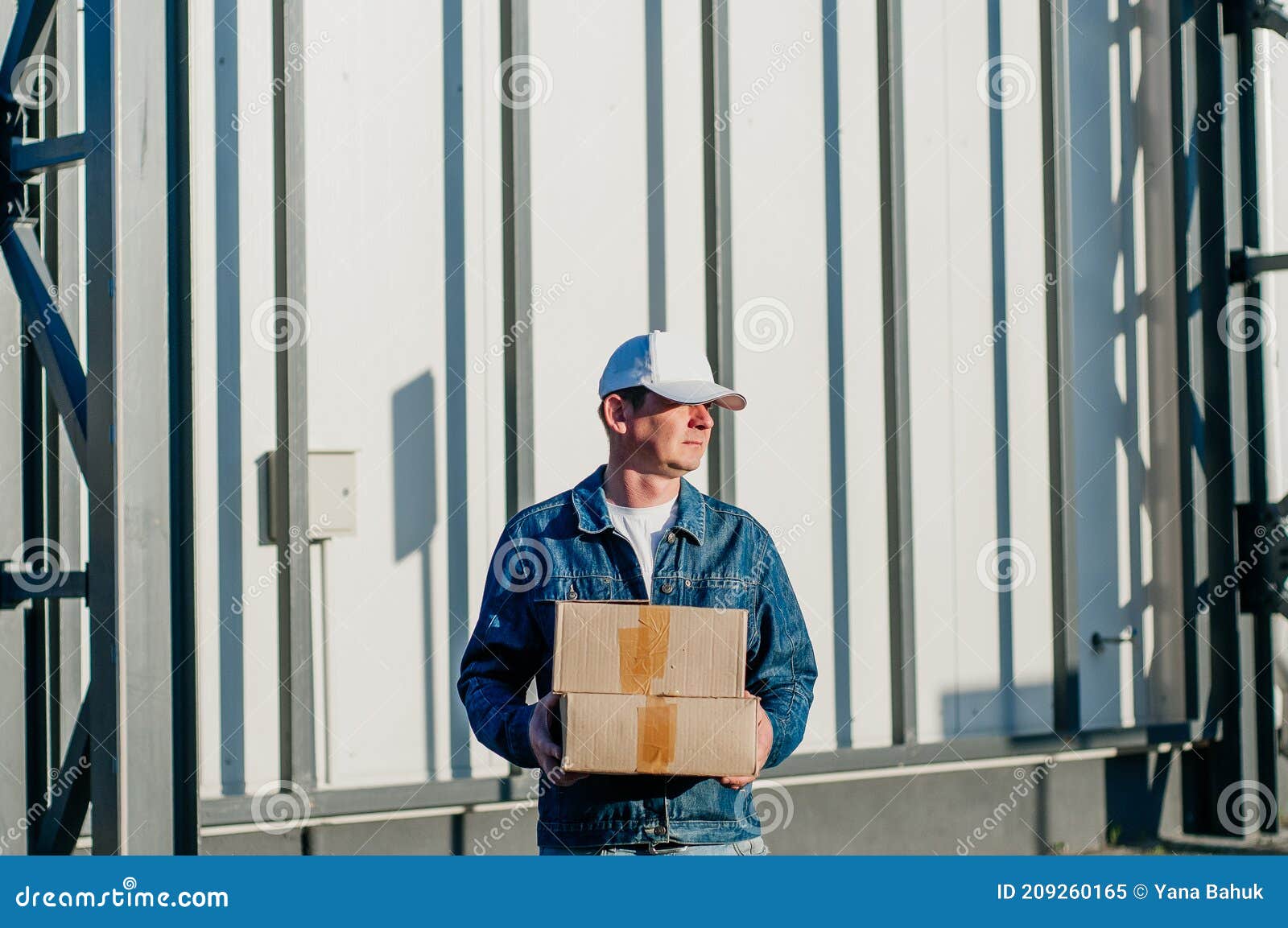 male courier in the blue costume and a cap taking out mail carton boxes from the white van on the sunny day in the street. outdoor