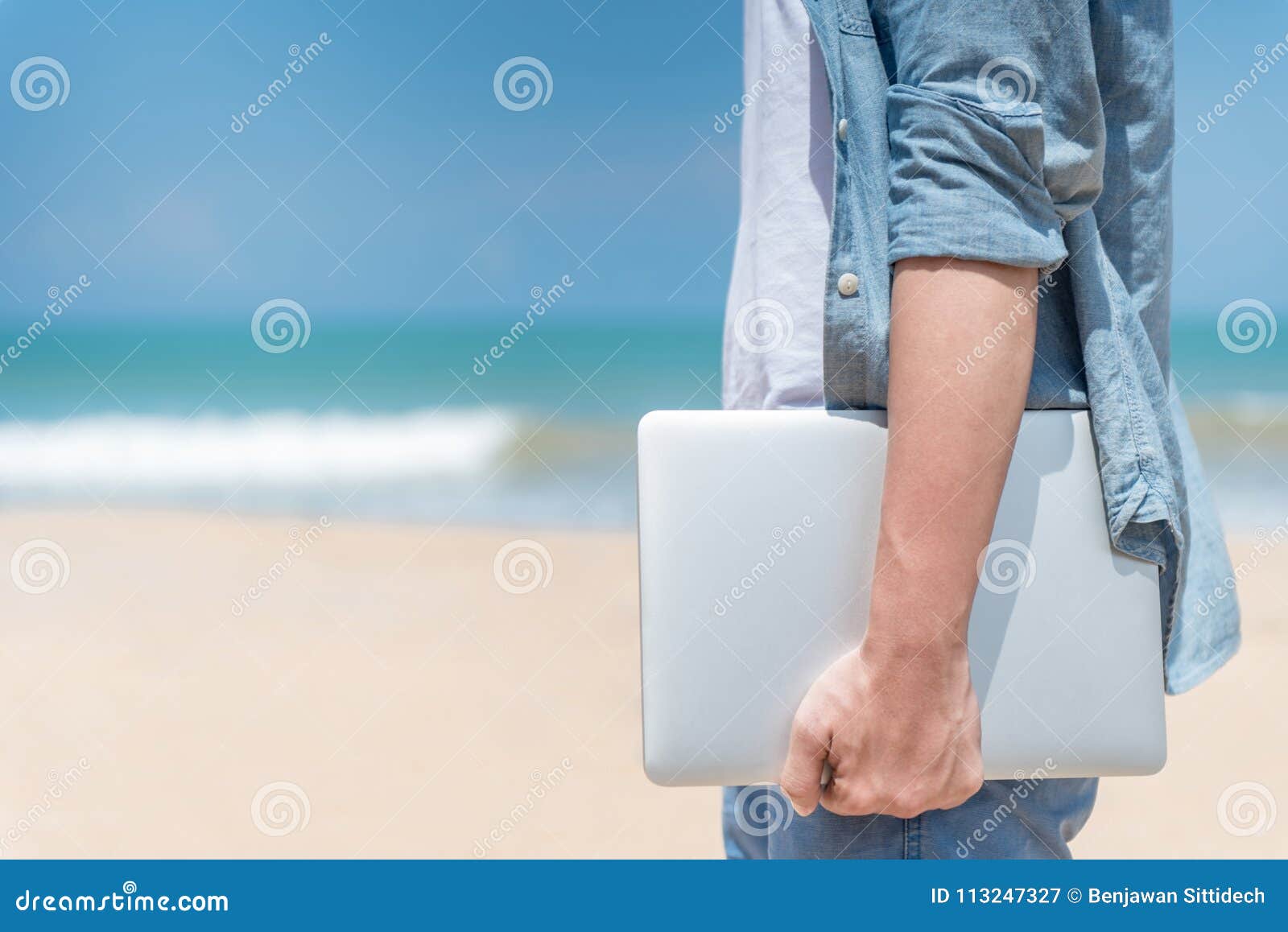 male digital nomad hand holding laptop on the beach