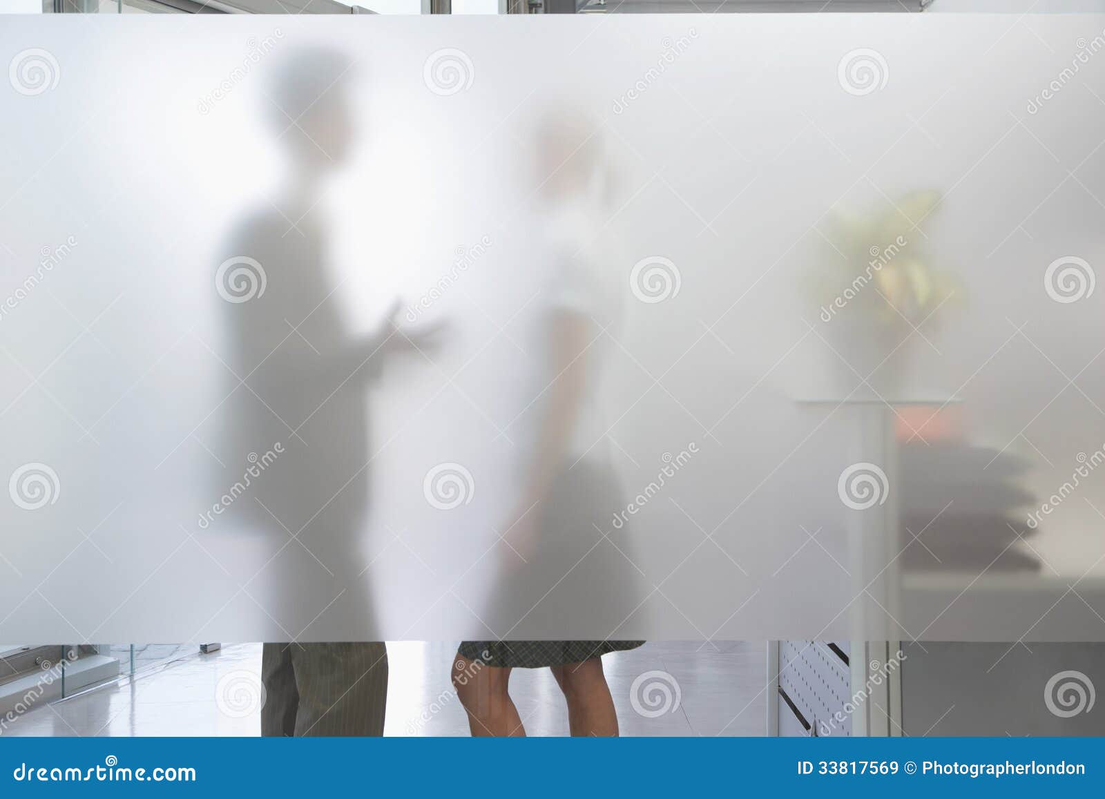 male executive talking to female colleague behind translucent wa