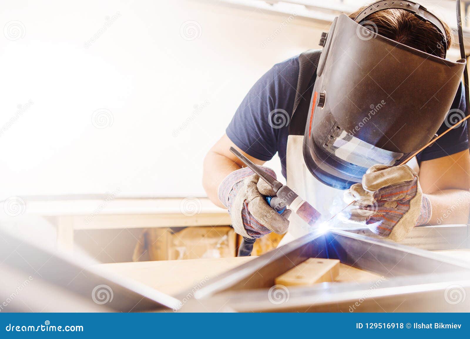 male in face mask welds with argon-arc welding