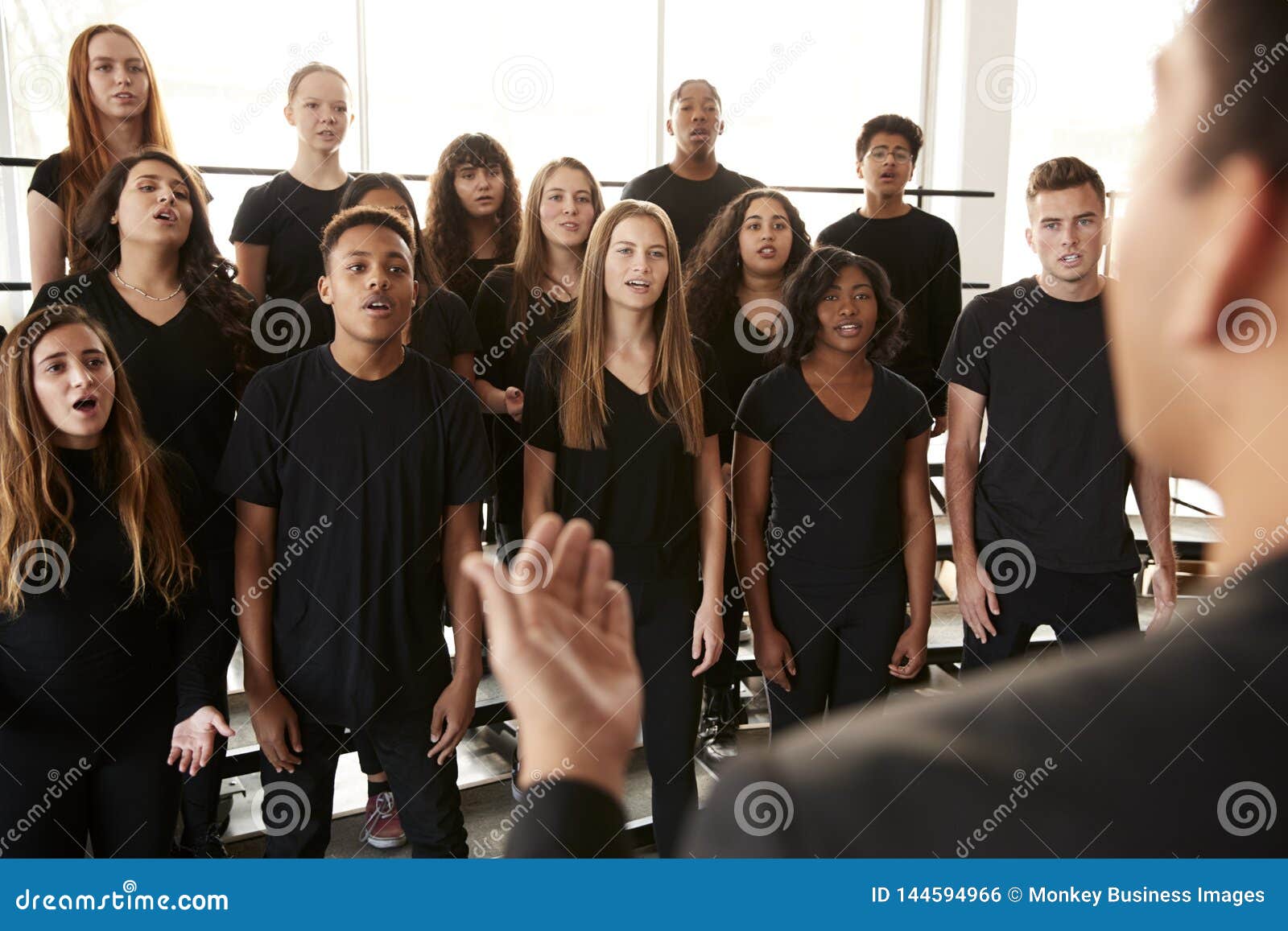 male and female students singing in choir with teacher at performing arts school