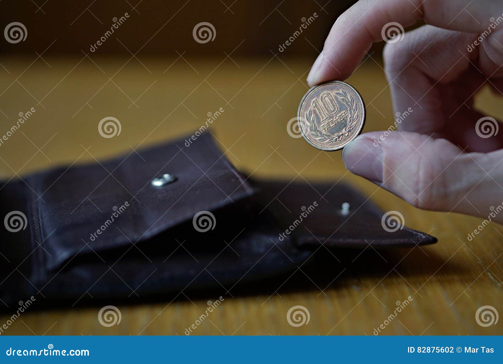 Male hand holding a bronze coin of ten Yens Japanese Yen, JPY and withdrawing that from the brown leather wallet
