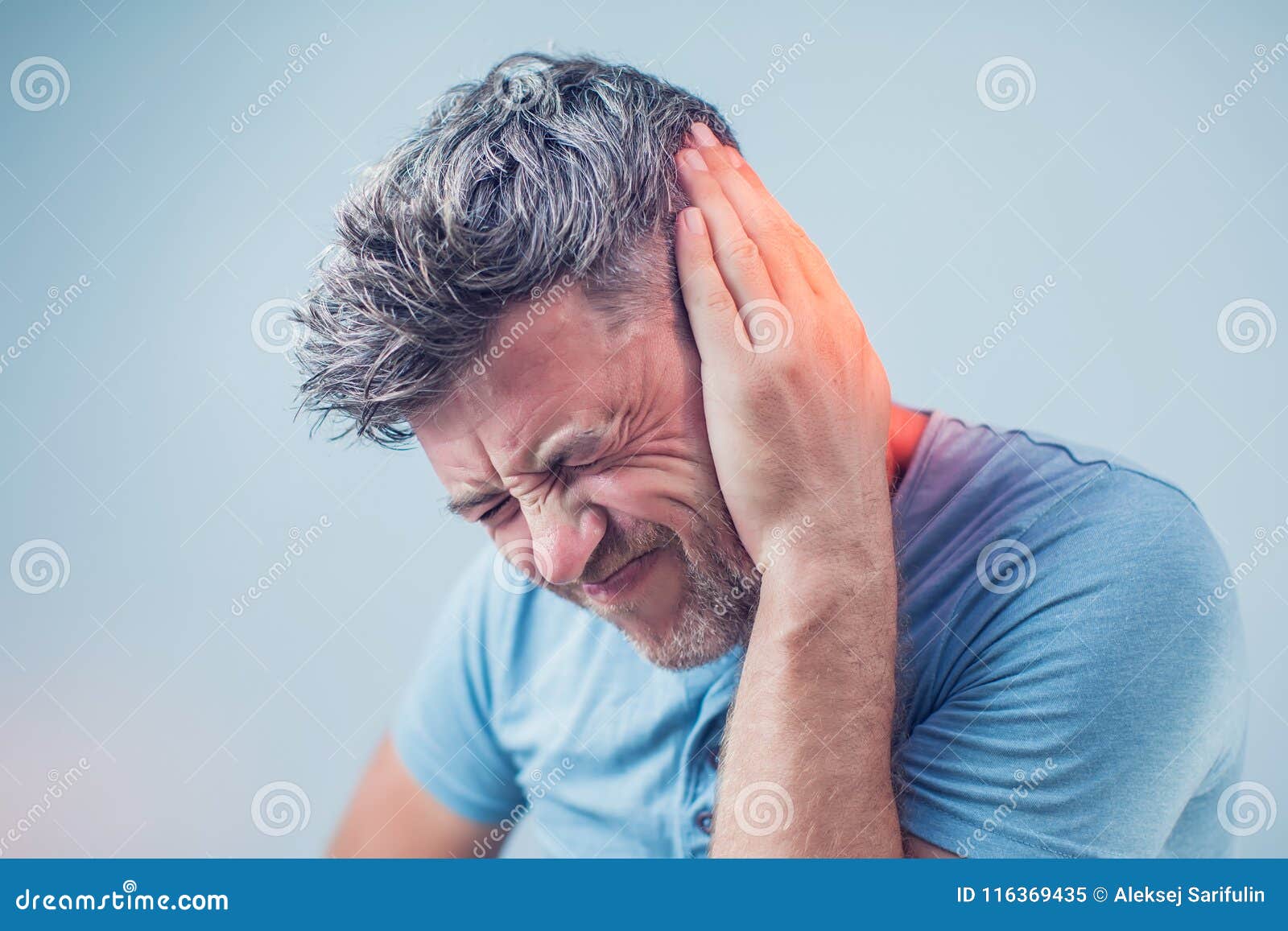 male having ear pain touching his painful head on gray