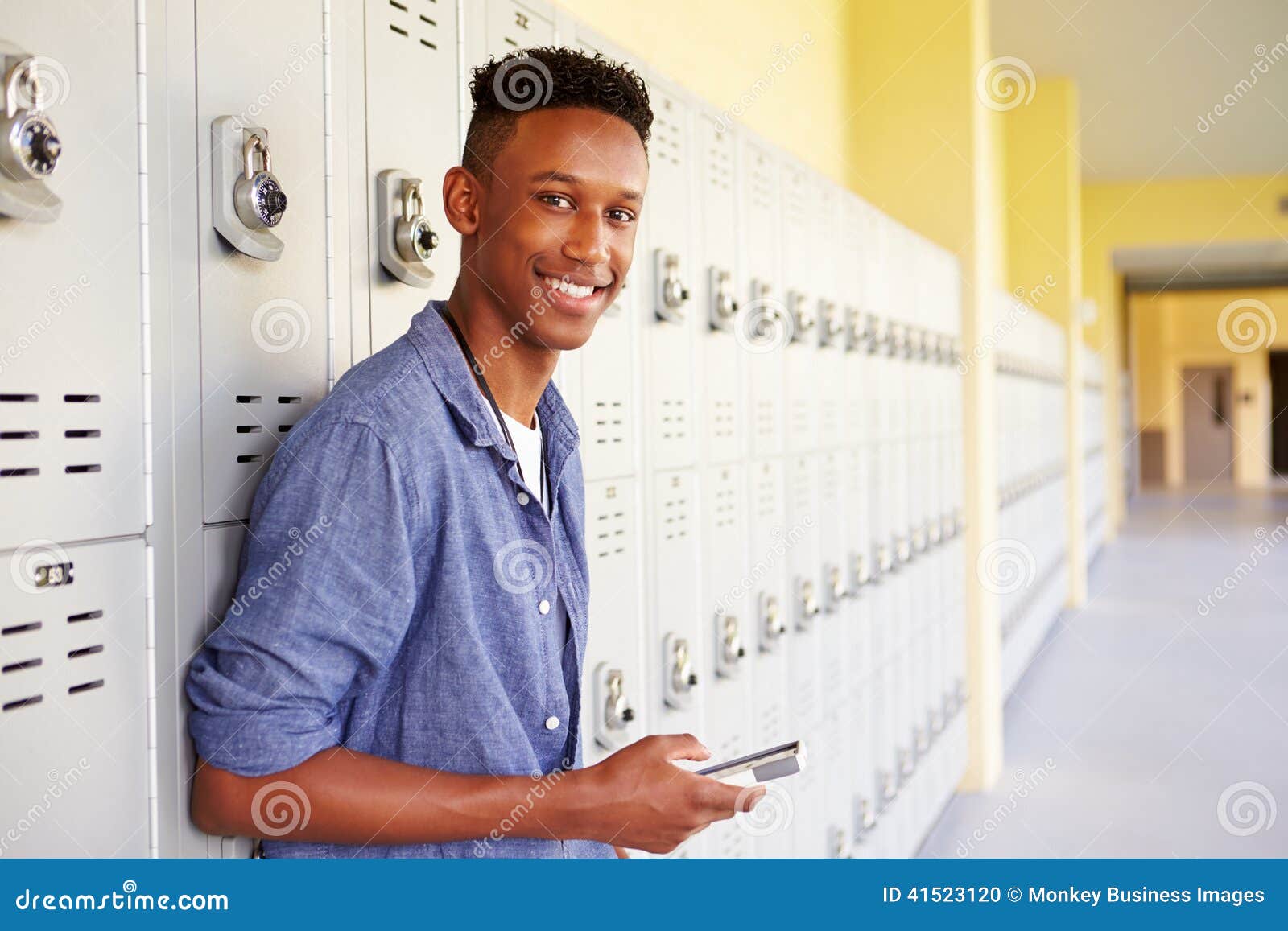 male high school student by lockers using mobile phone