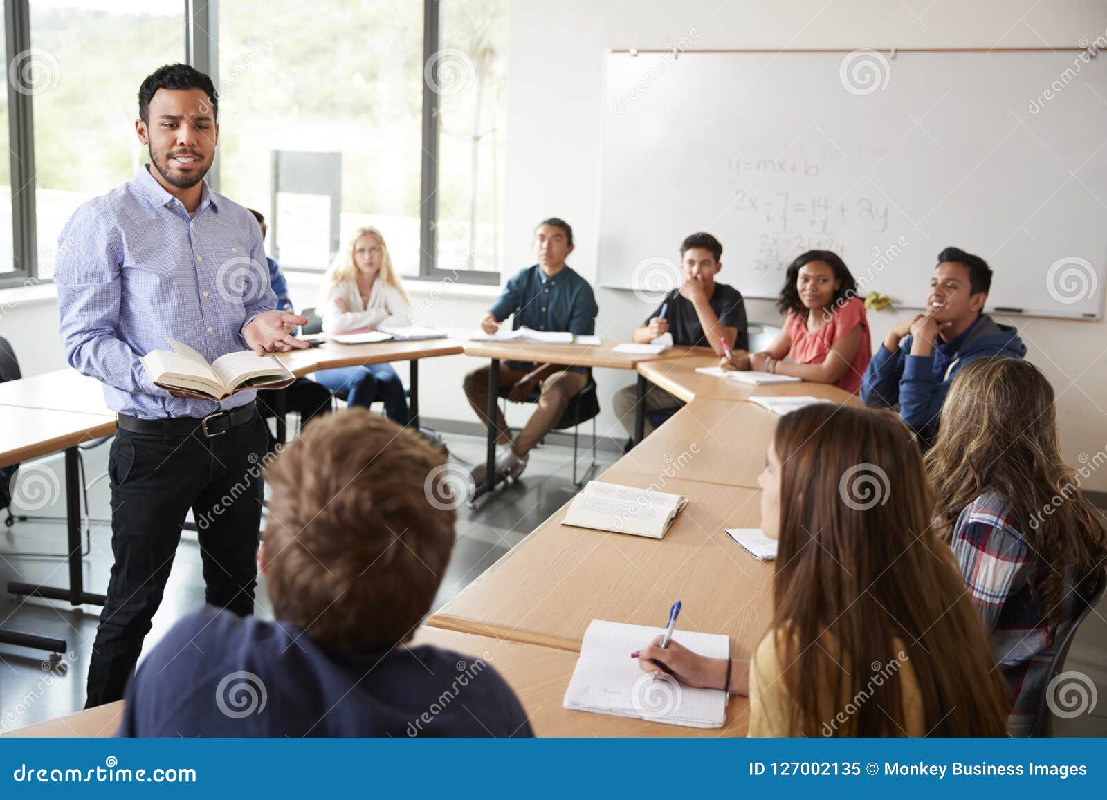 male high school tutor with pupils sitting at table teaching maths class