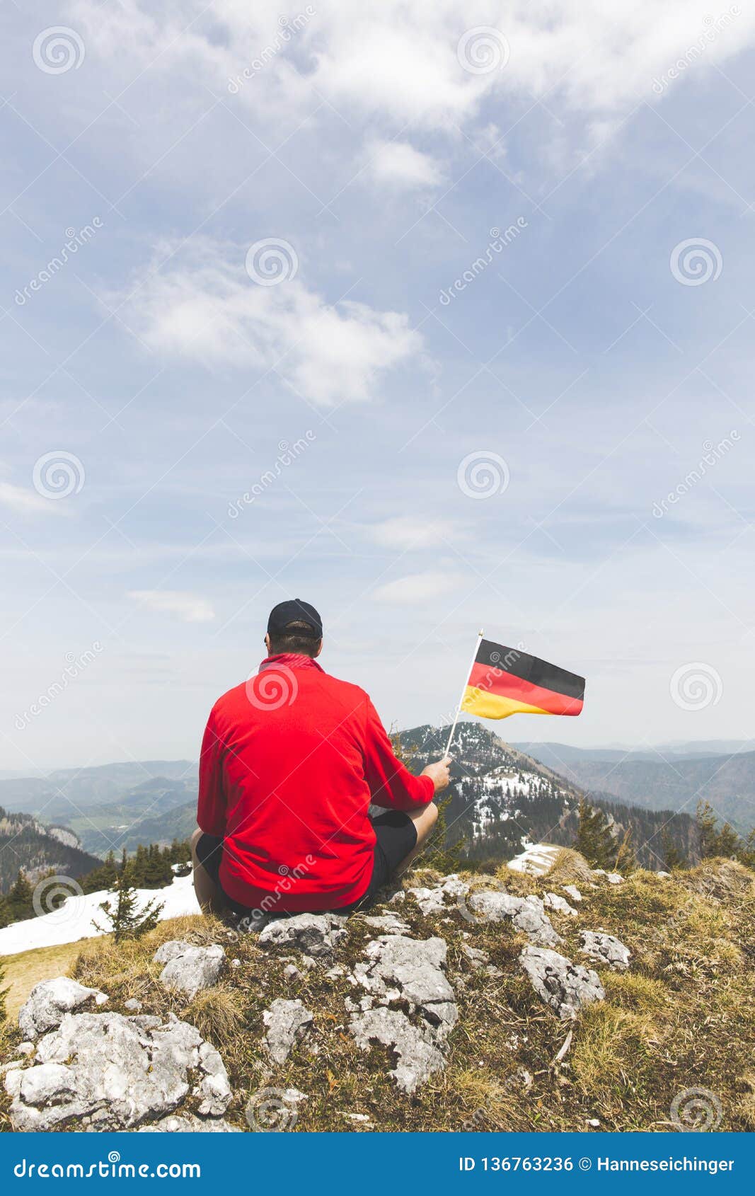 Male Hiker With Red Sweater Is Holding A German Flag In The Mountains