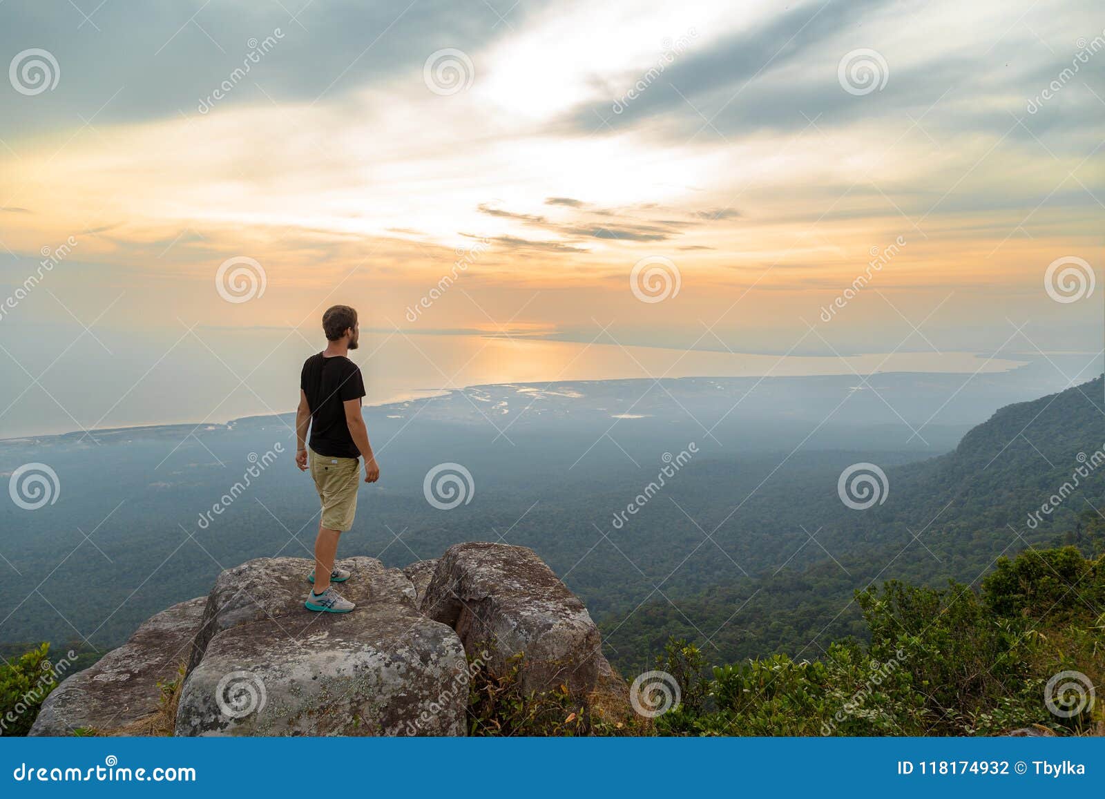 Male hiker on top of the mountain enjoying valley view. Lonely young man stands on the mountain and looking into the distance, Kampot, Cambodia