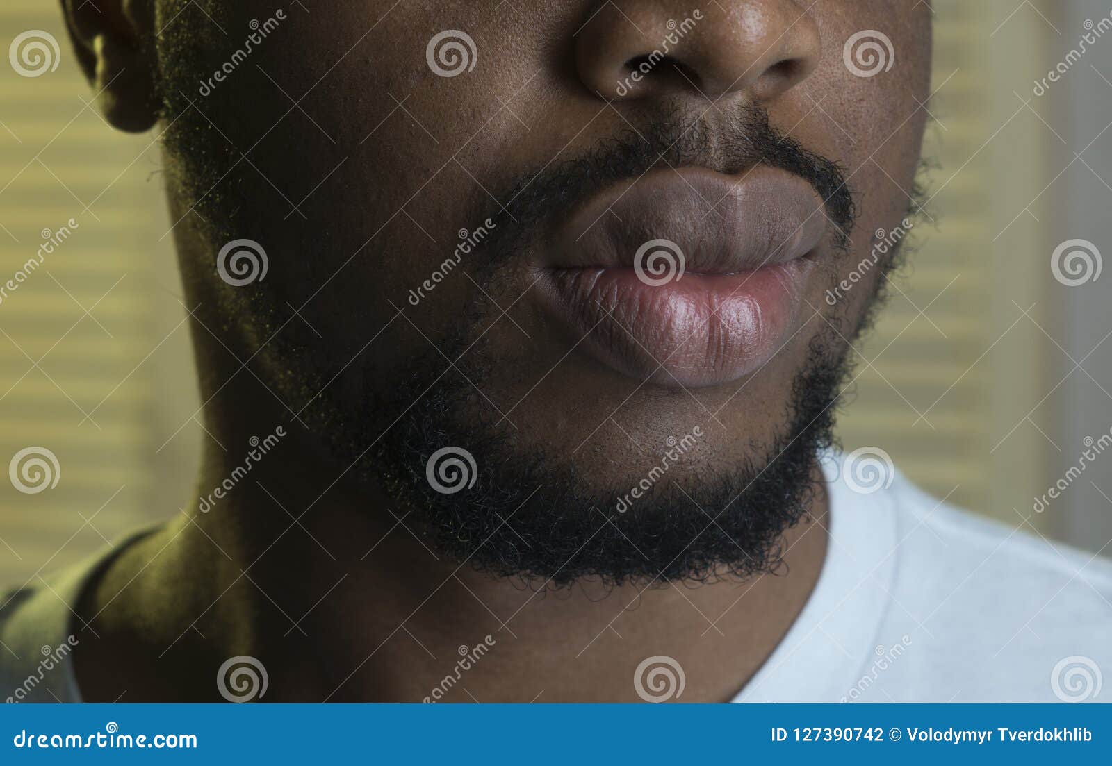 Rapper culture concept. Black macho with beard wears rapper cap and looks  handsome. Man on calm face with sensual big lips, close up. Man with beard  and mustache indoor, jalousie background Stock