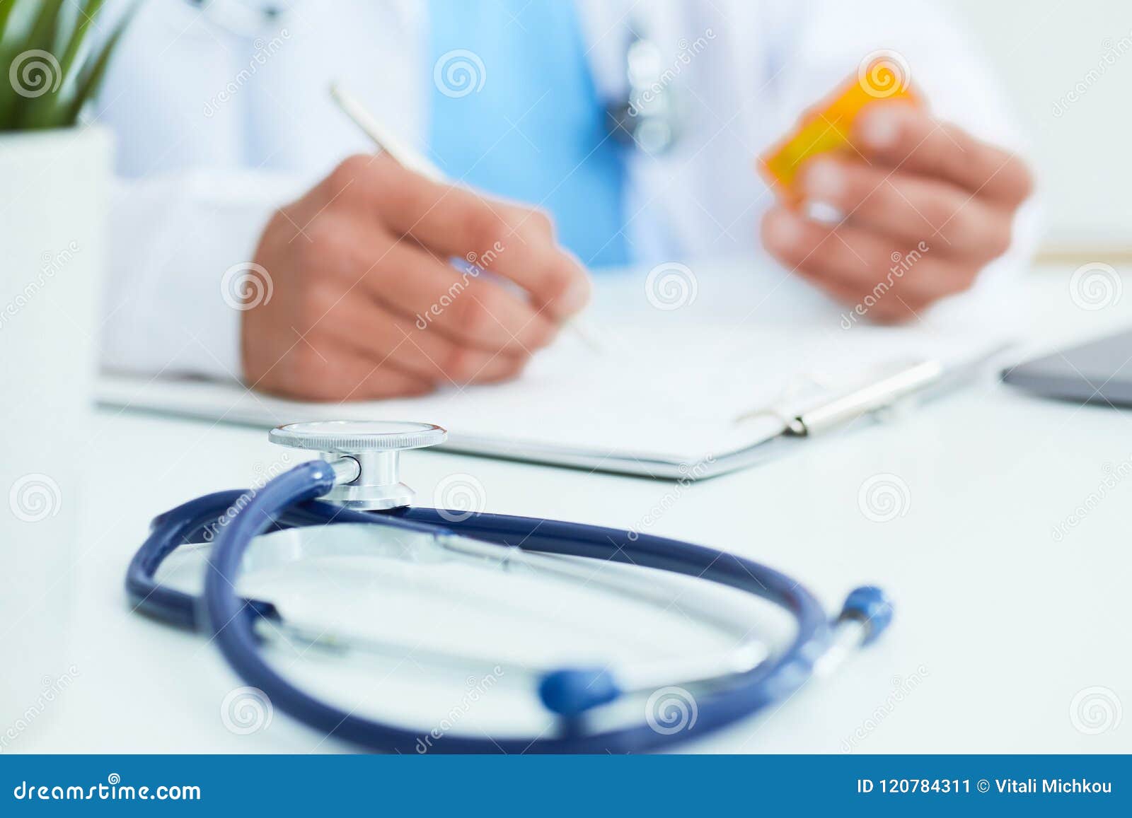 male physician medicine doctor or pharmacist sitting at worktable, holding jar or bottle of pills in hand and writing