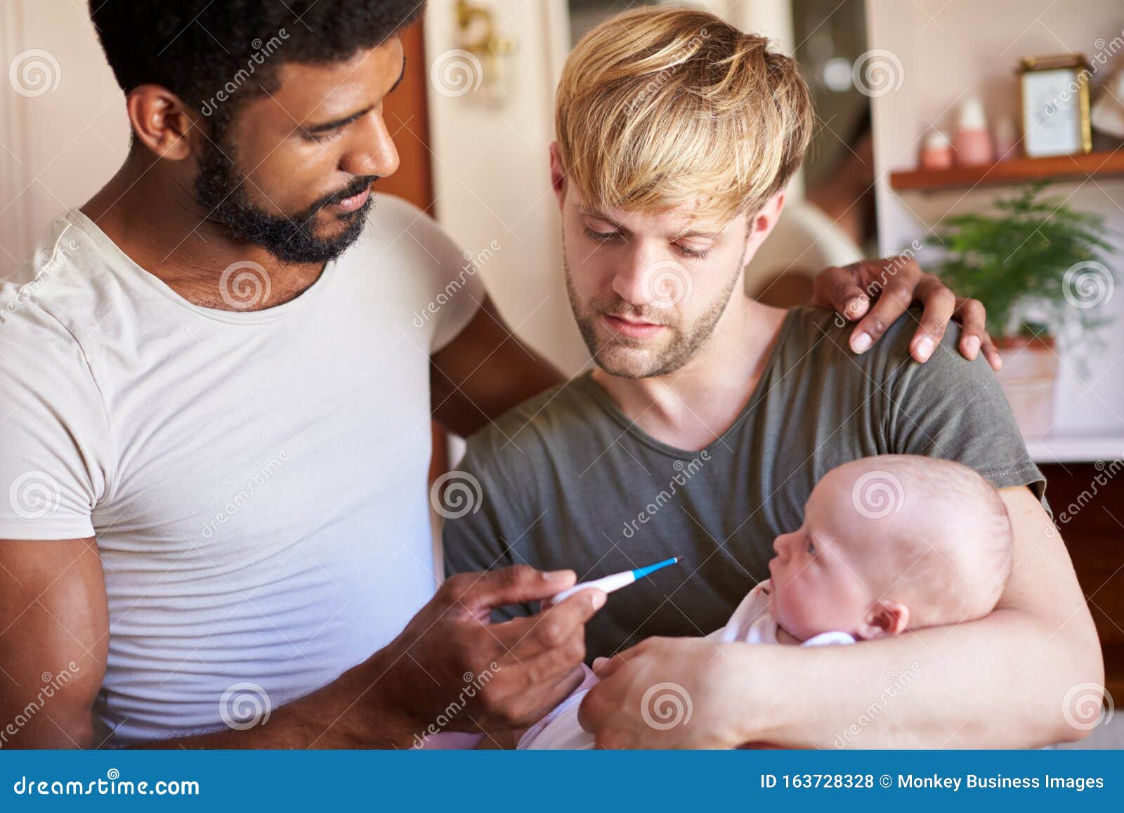 Male Same Sex Couple Checking Baby Daughters Temperature in Bathroom at Home Stock Photo