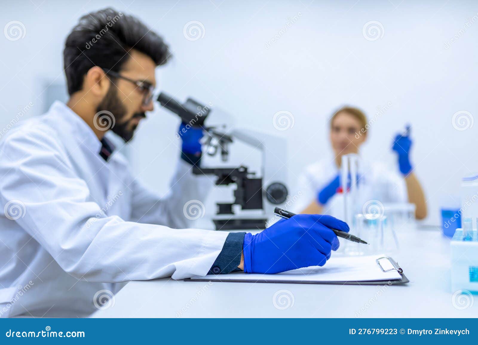 male scientist working with microscope, doctor's team in laboratory doing research, making notes