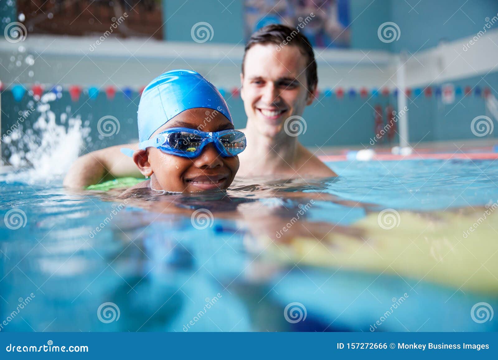 male swimming coach giving boy holding float one to one lesson in pool