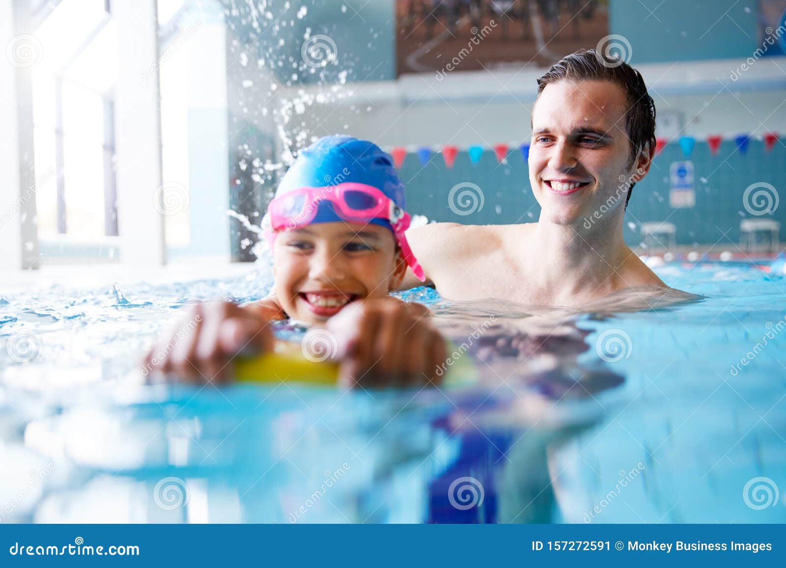 male swimming coach giving girl holding float one to one lesson in pool
