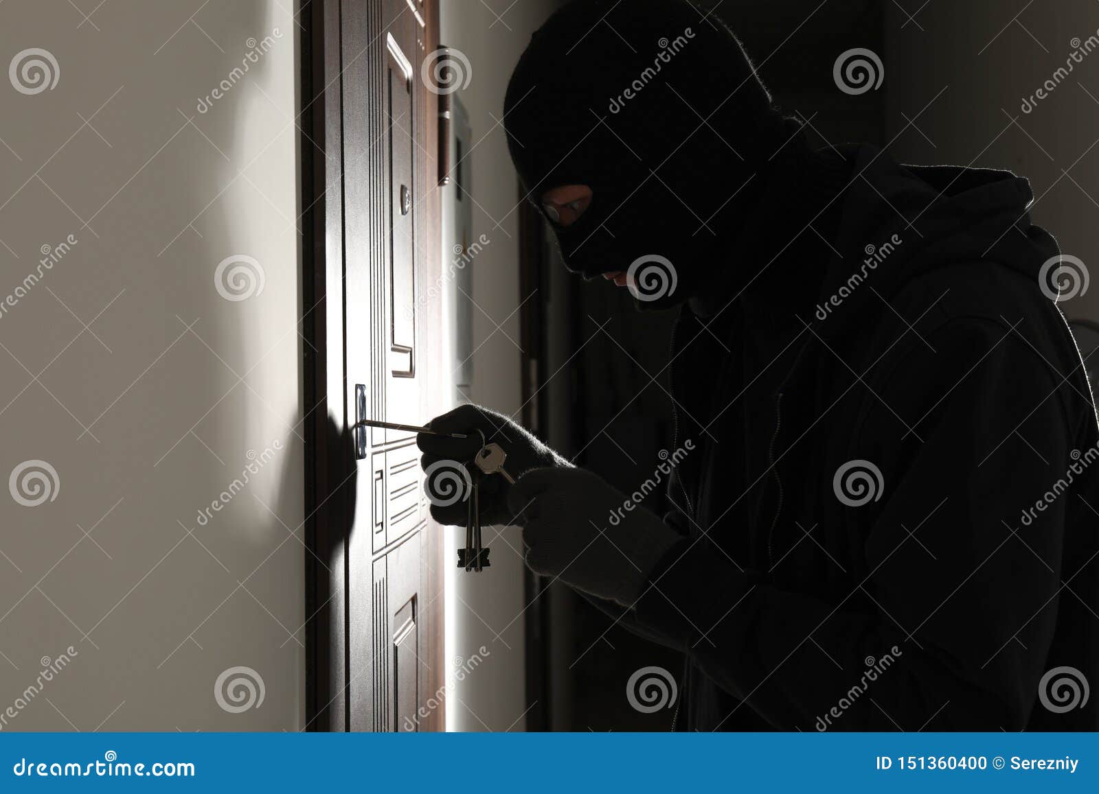 male thief opening door with keys indoors